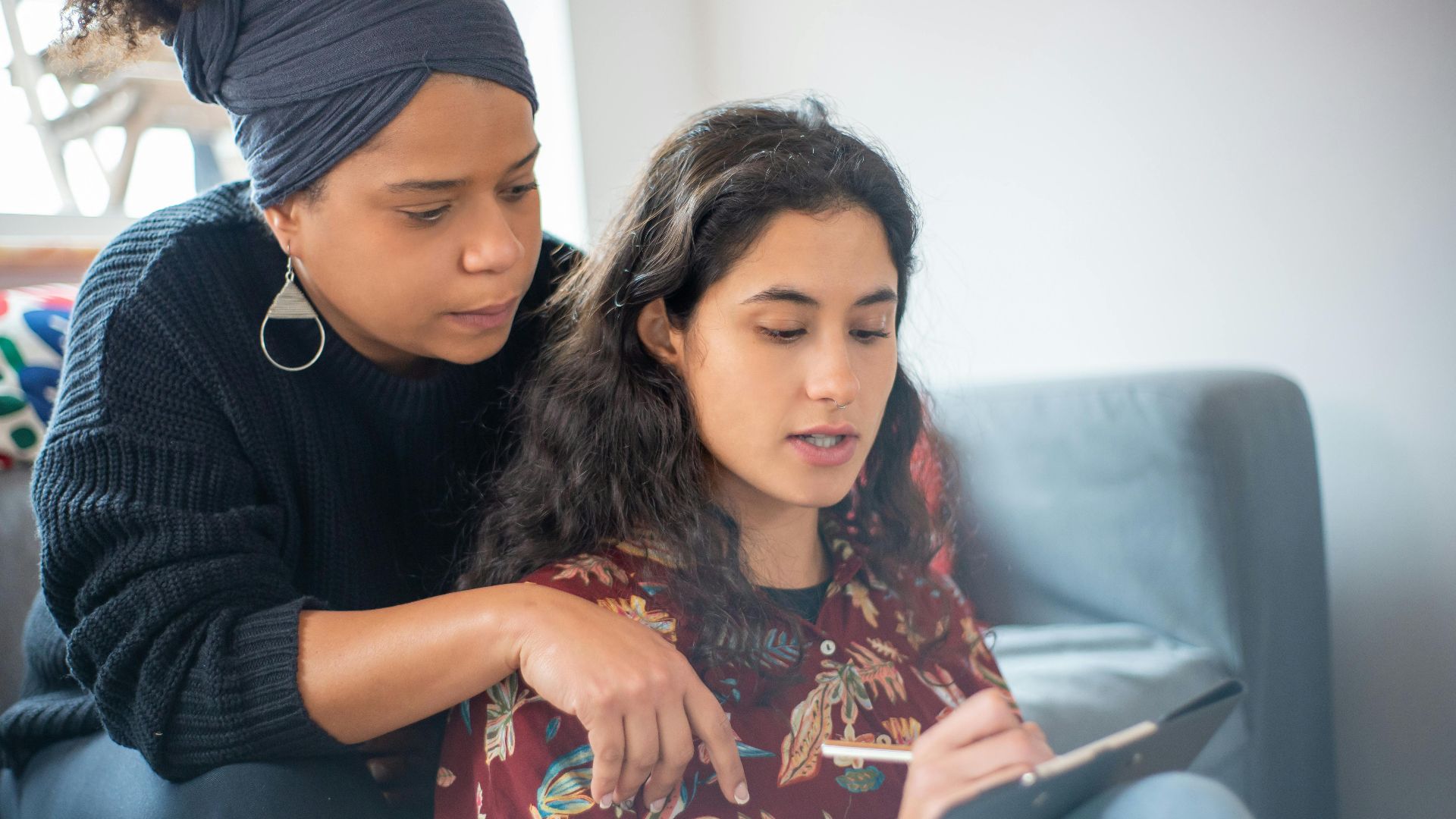 Two women sitting on a sofa sharing a thoughtful moment, one writing or drawing.