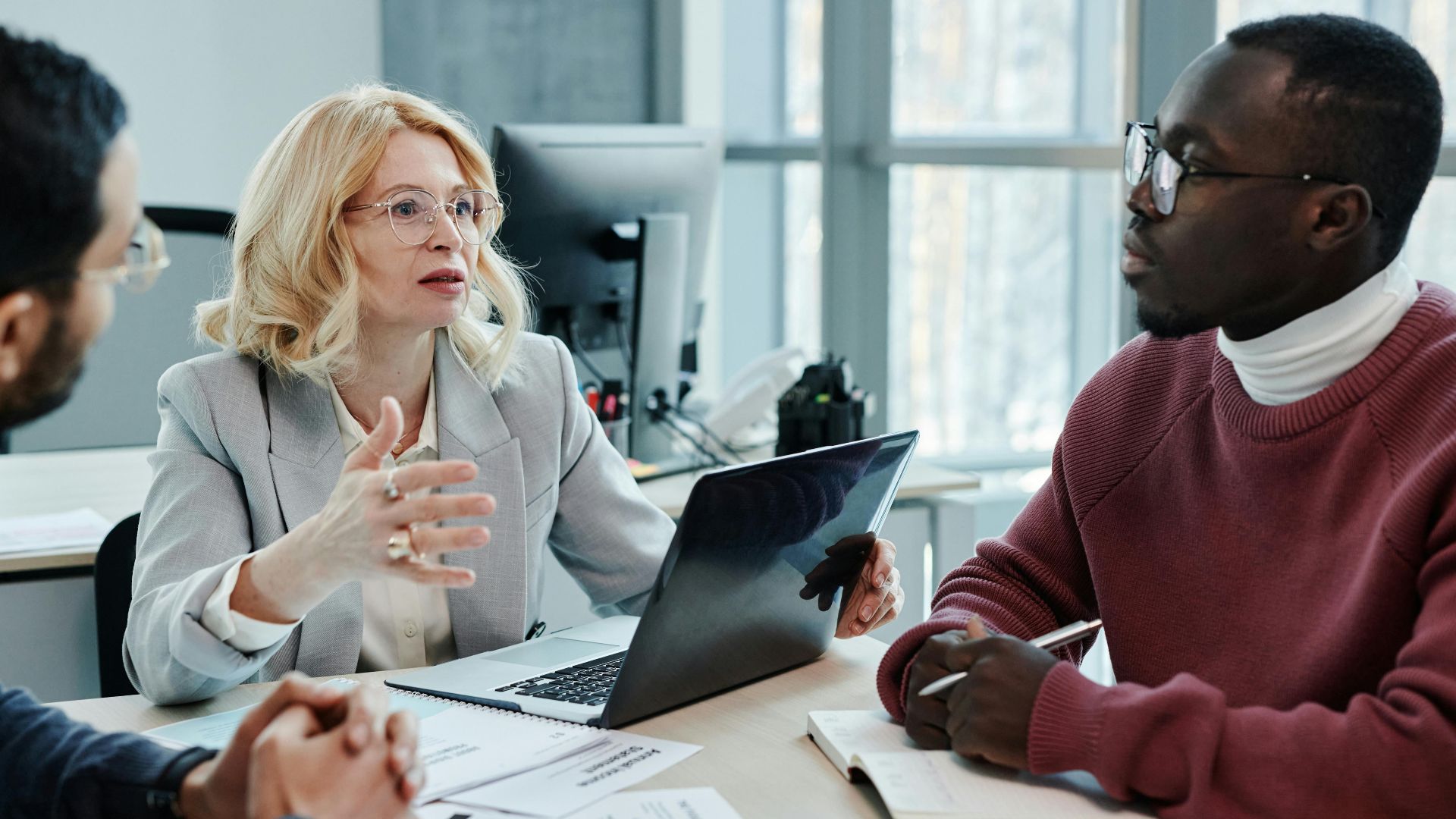 Business professionals discussing strategy around a table with a laptop in an office setting.
