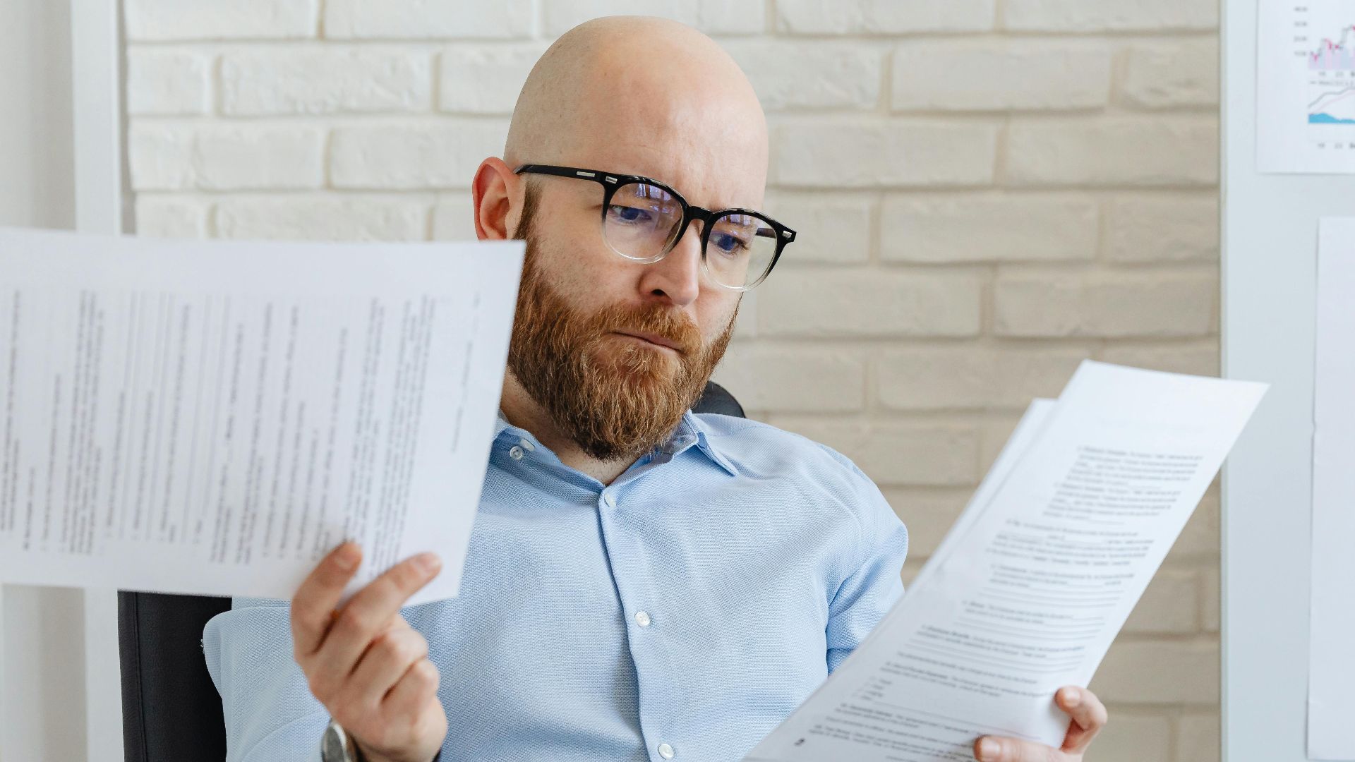 Bald bearded businessman reading financial documents in modern office setting.