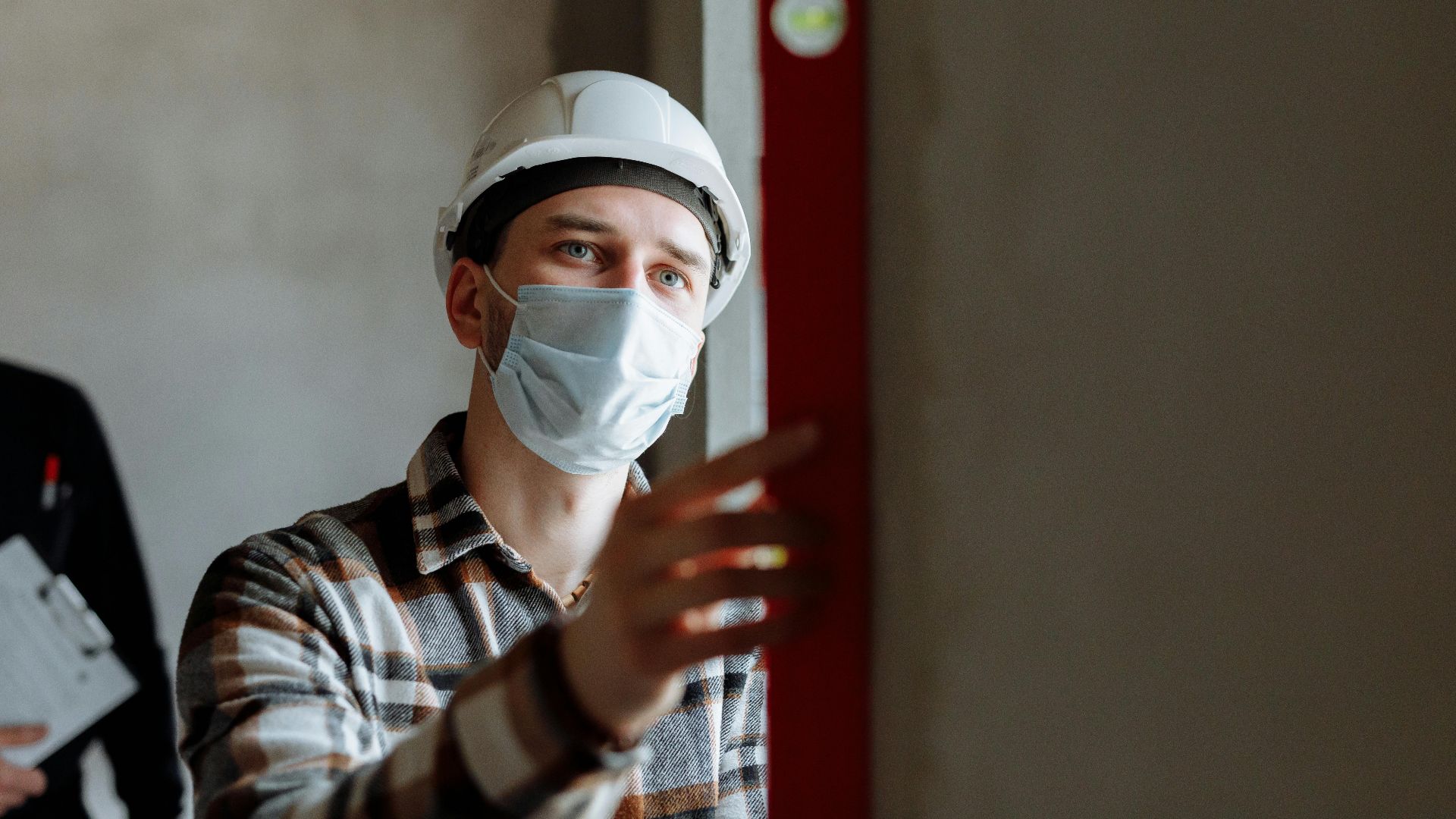 Man wearing a face mask and hard hat conducting safety inspection indoors.