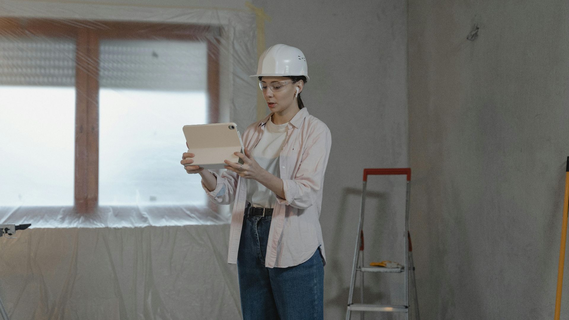 Woman in hard hat using tablet for construction project in unfinished interior.