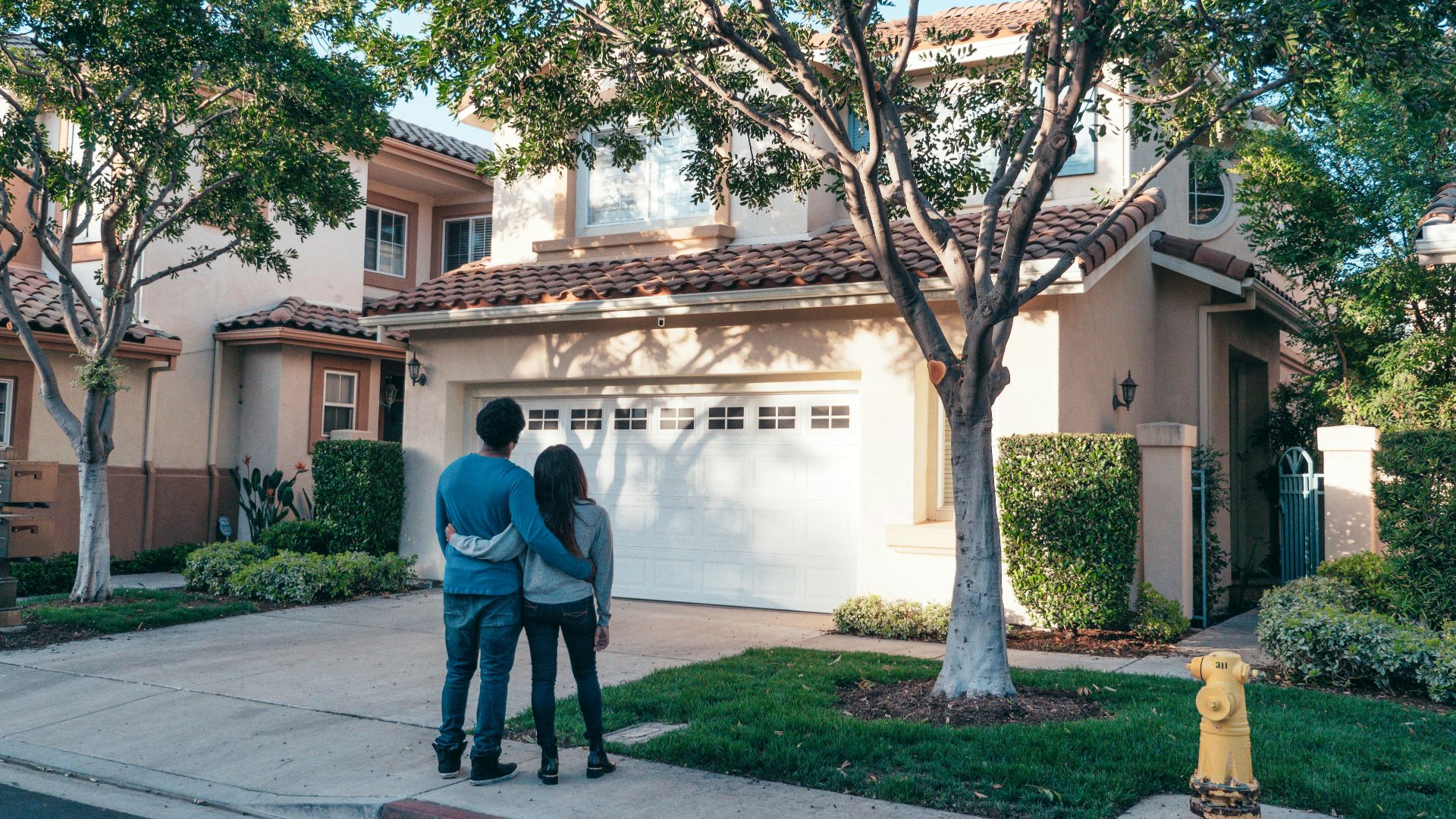 Couple hugging outside their newly purchased suburban home, showcasing togetherness and new beginnings.