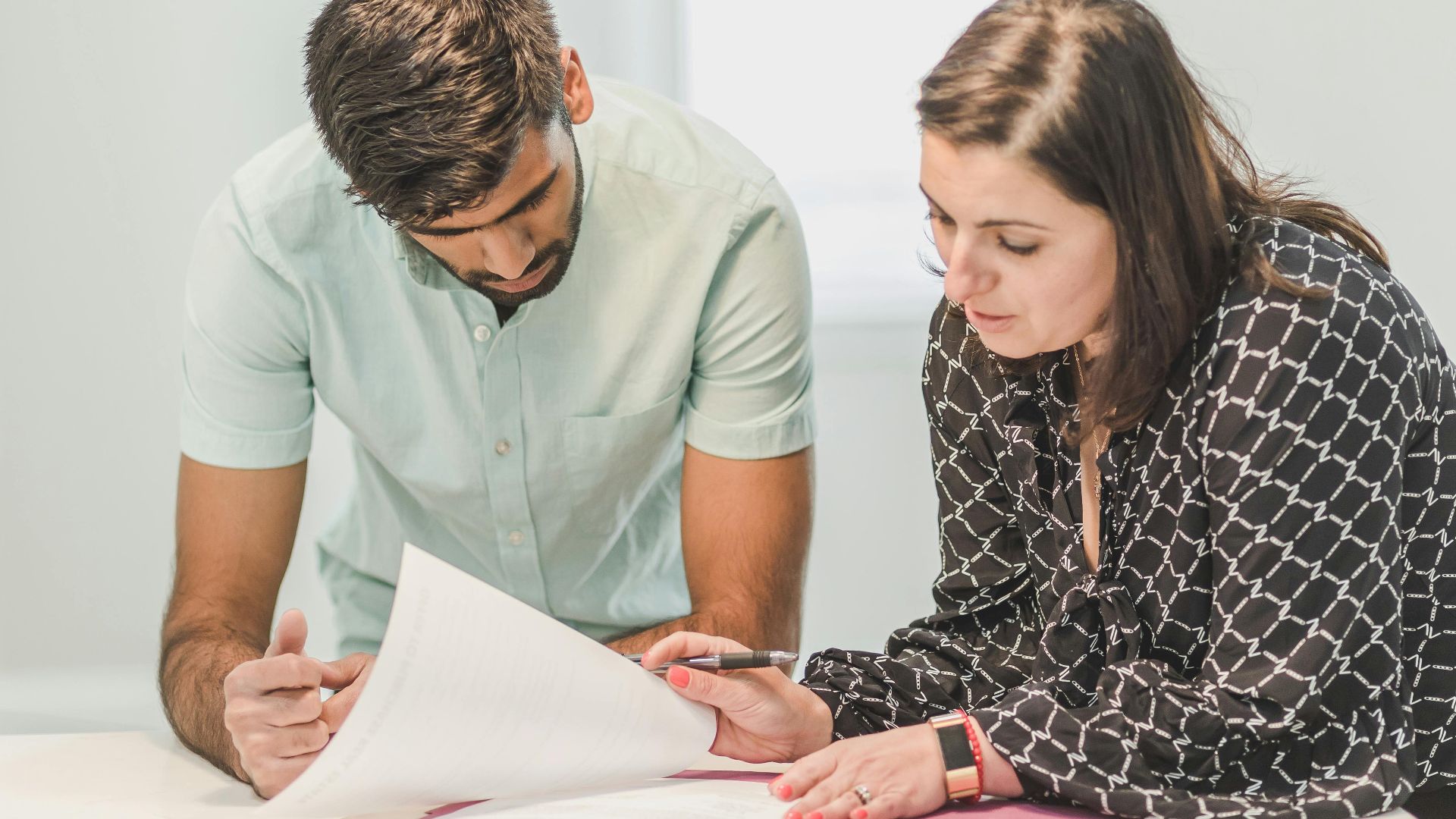 Real estate agent assisting first-time homebuyer with documents inside a bright room.