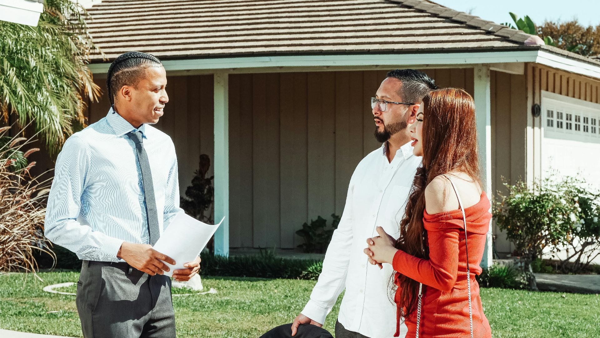 A real estate agent discusses property details with a couple outside a suburban home.