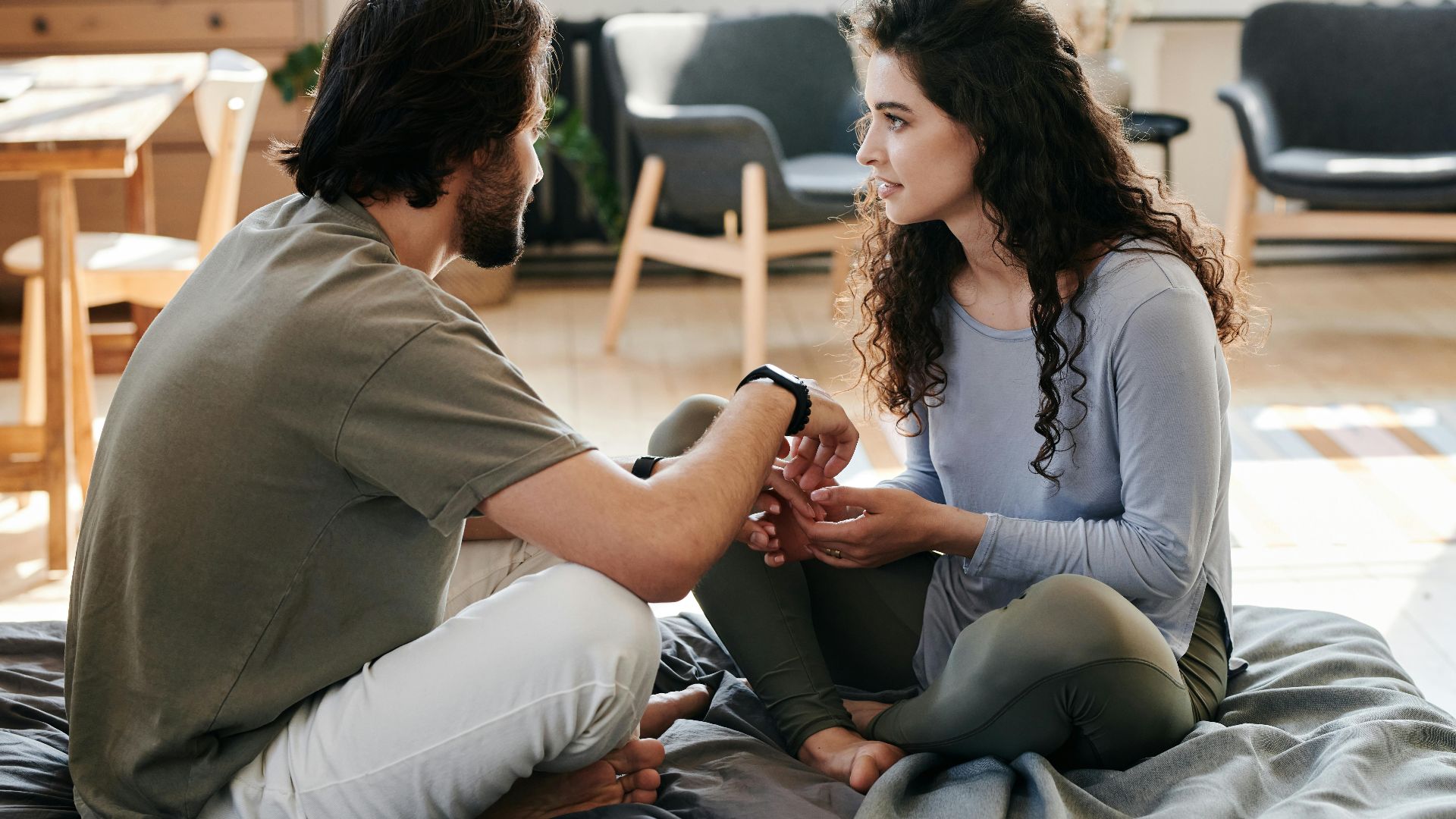 A couple sitting closely on a bed, engaged in a thoughtful discussion in a cozy home setting.