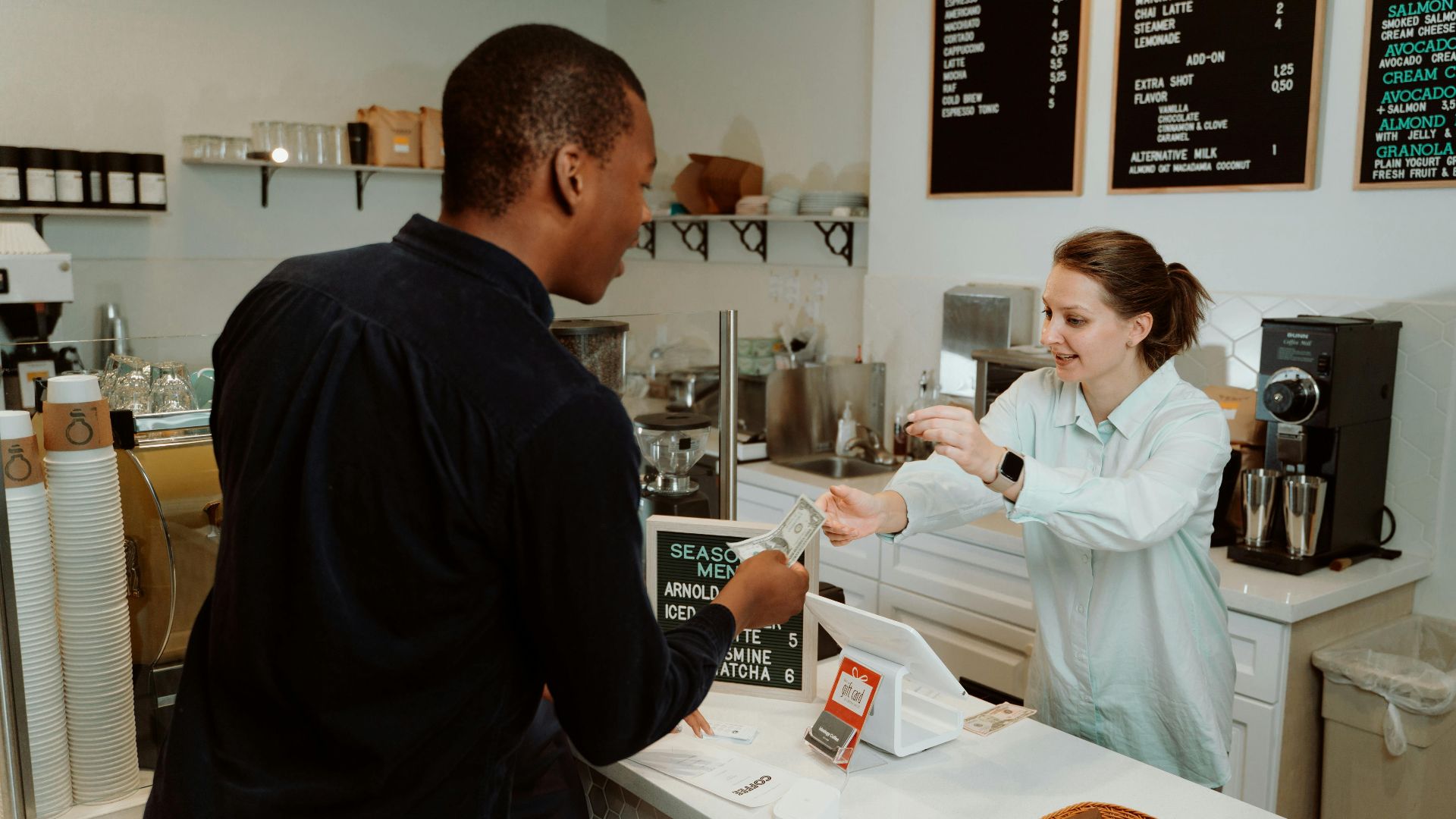 A customer pays for coffee at a café counter, transaction with barista.