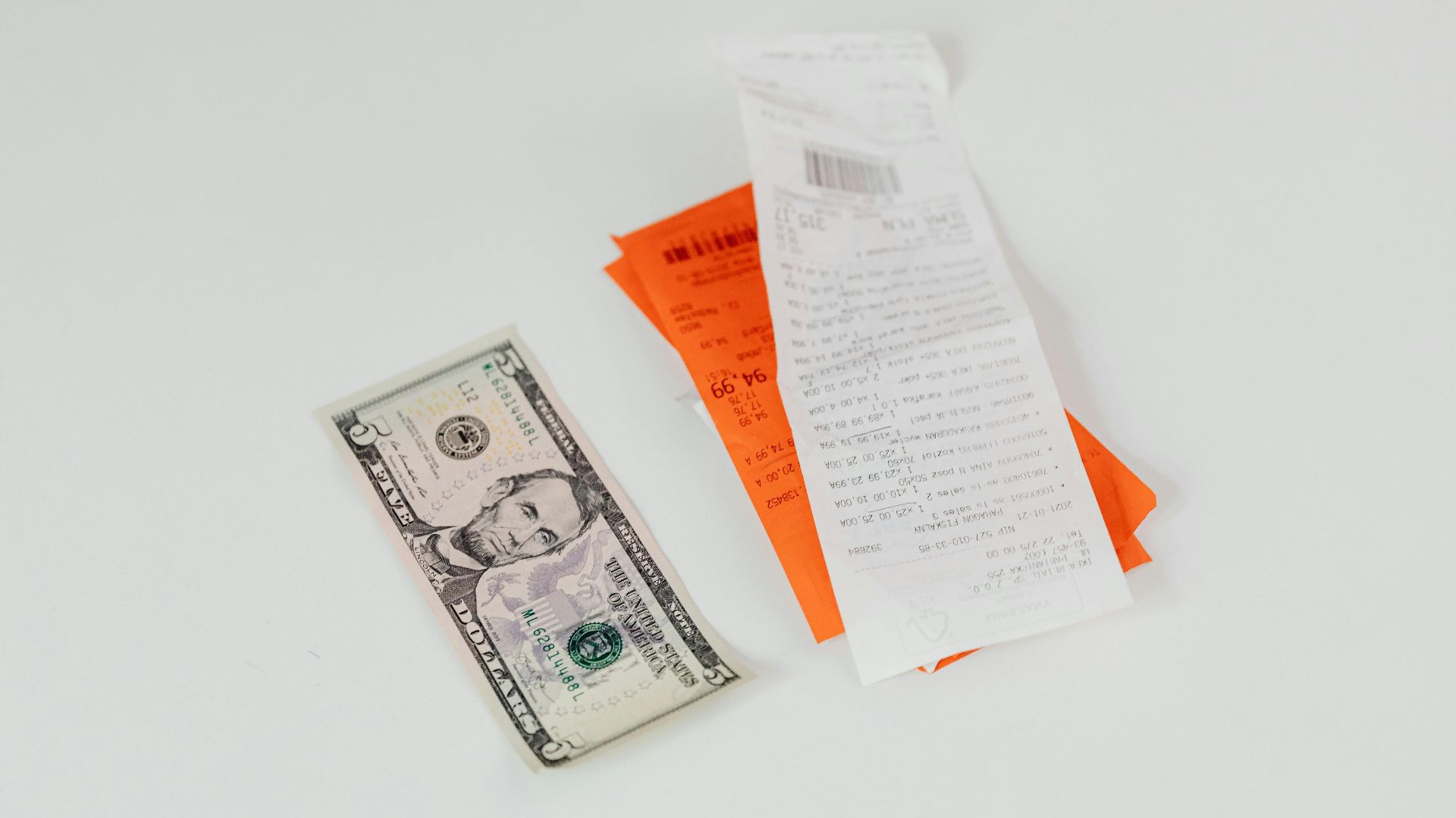 Close-up of a five-dollar bill next to shopping receipts on a white background, ideal for finance and retail themes.