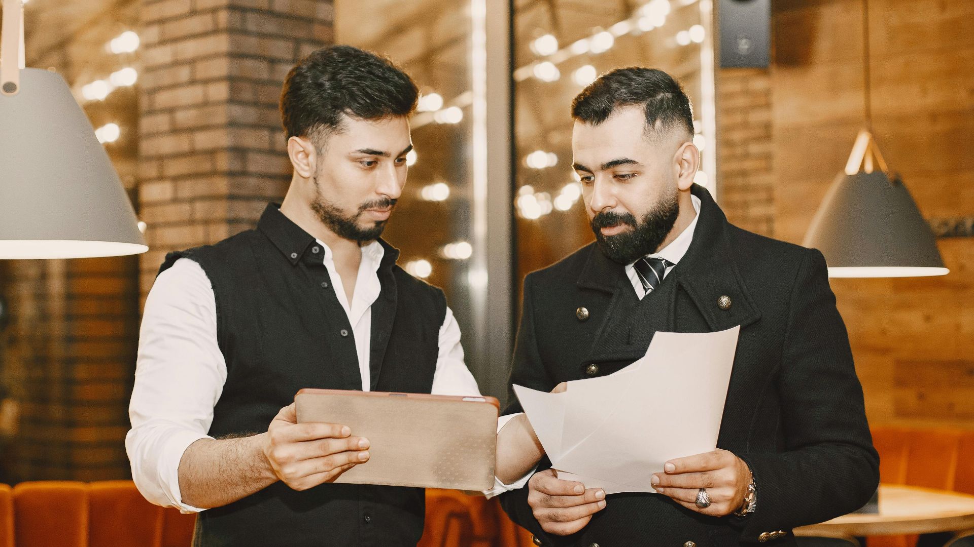 Two businessmen reviewing documents and a tablet in a modern indoor setting.