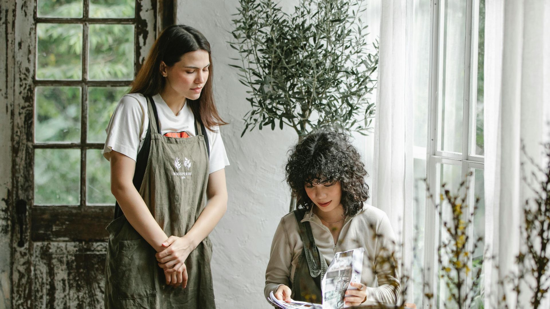 Young waitress waiting for focused female client turning pages of menu while making order in cafe