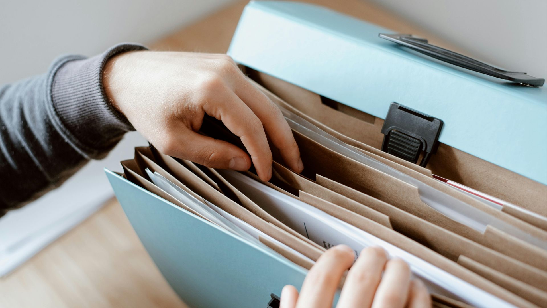 Crop unrecognizable person selecting document in opened briefcase for documents placed on wooden table