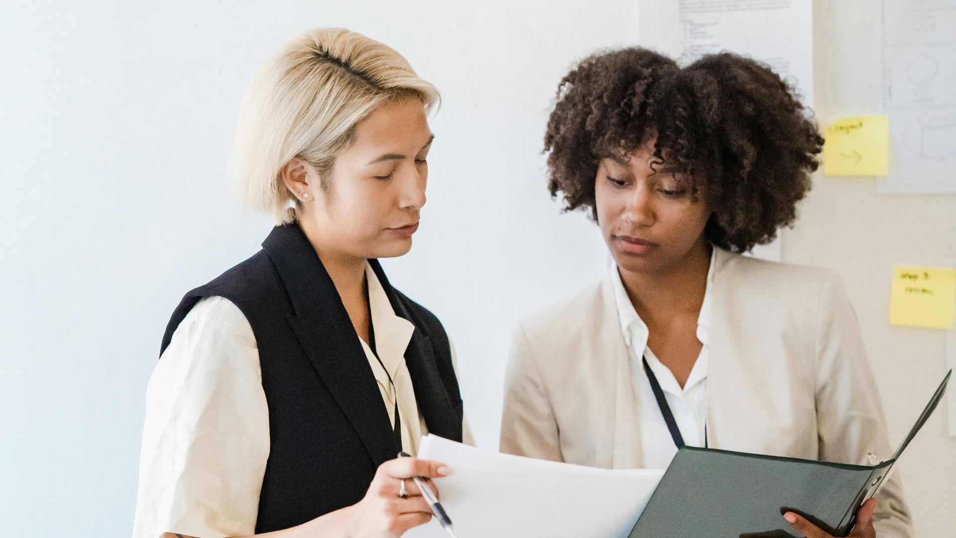 Two businesswomen engaged in discussion and document review in an office setting.