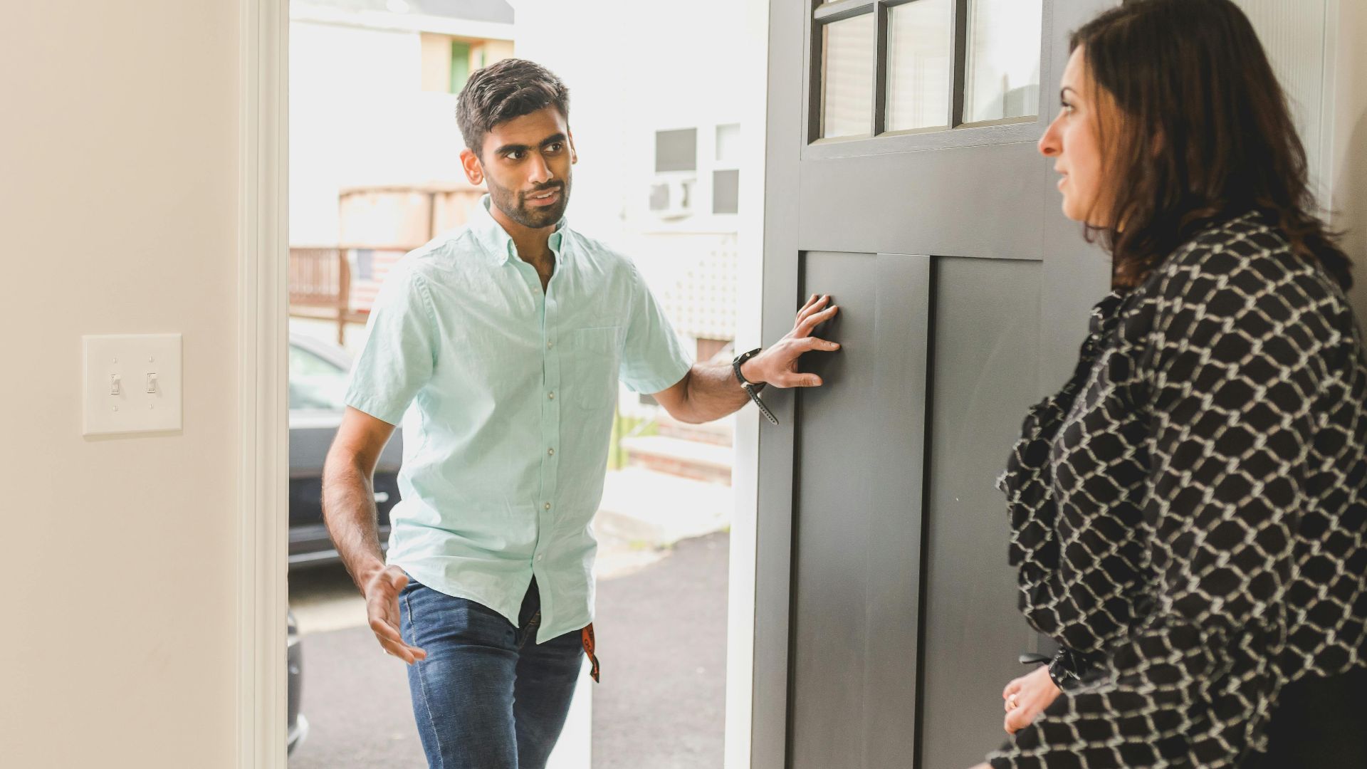 A man enters a home, conversing with a woman standing nearby in a casual setting.