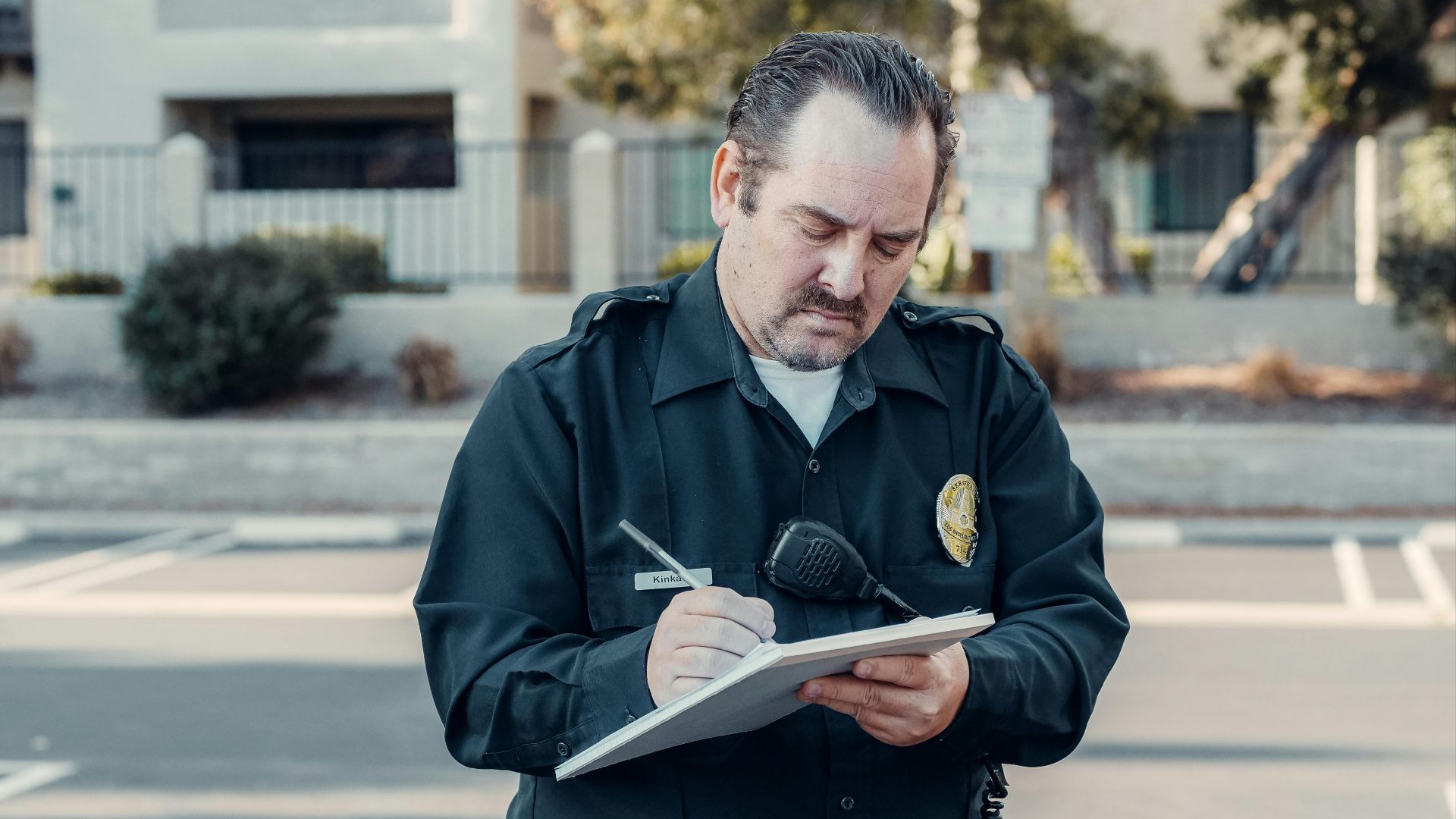 Police officer in uniform writing a ticket on a clipboard outdoors.