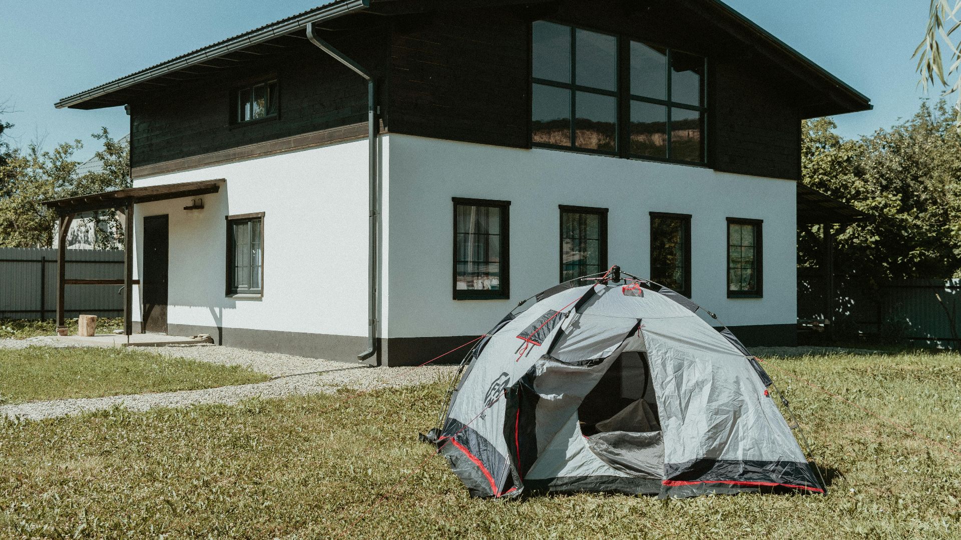 A modern two-story house with a pitched roof and a camping tent in the grassy garden.