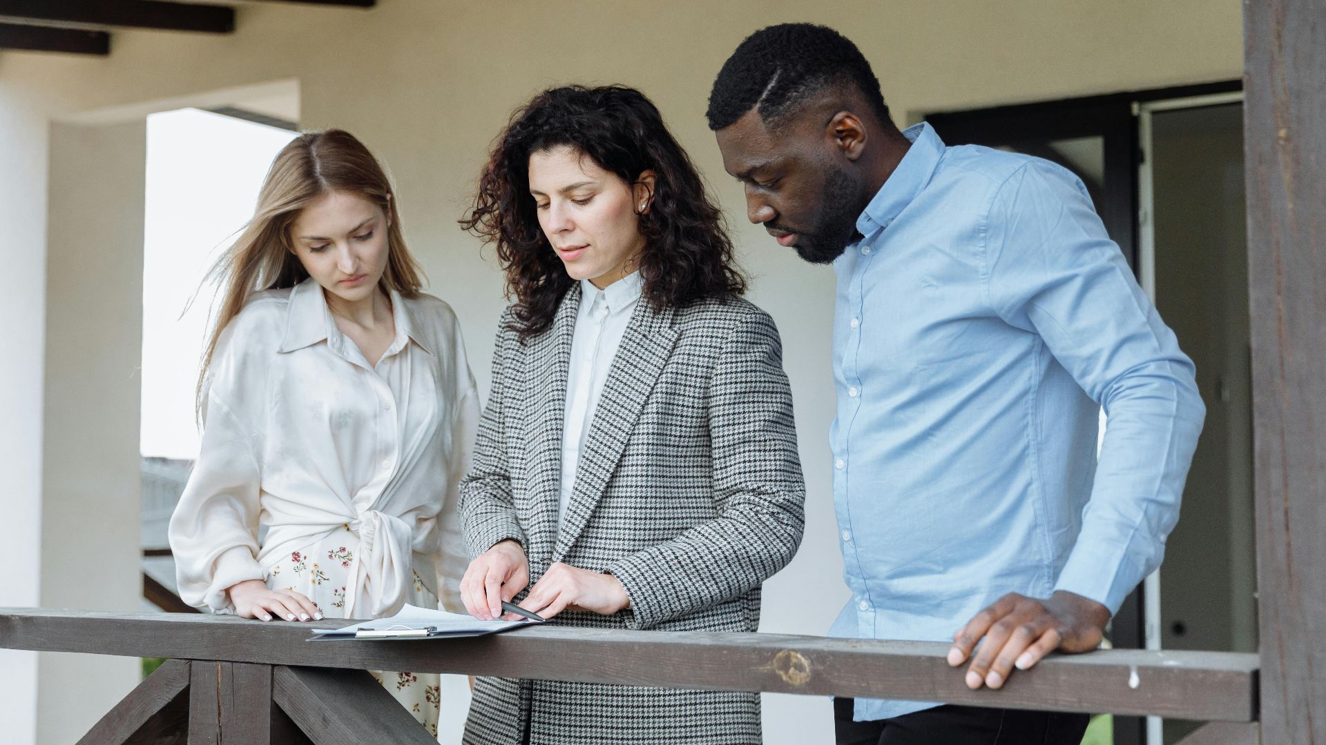 Three adults reviewing documents on a balcony during a real estate consultation.