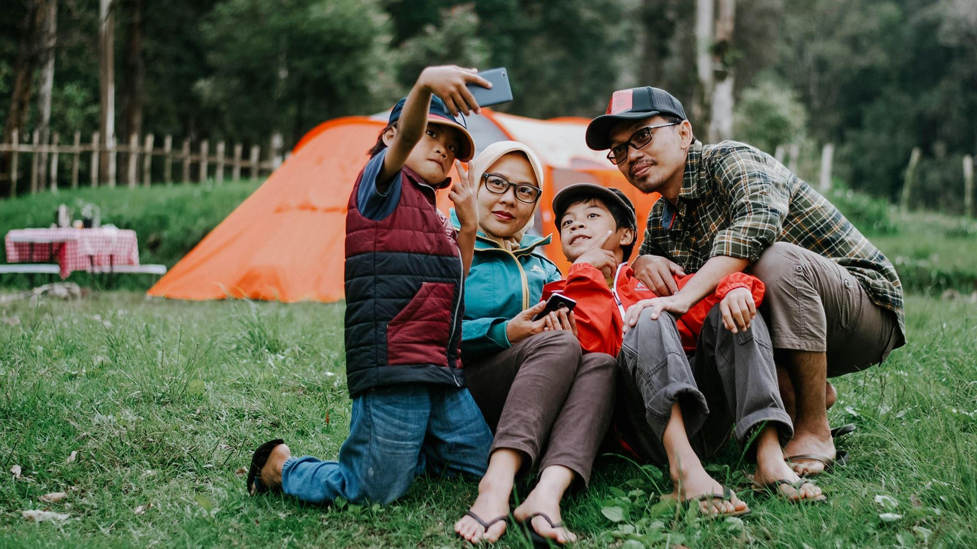 Family enjoying a camping trip, taking a selfie in front of their tent during the day.