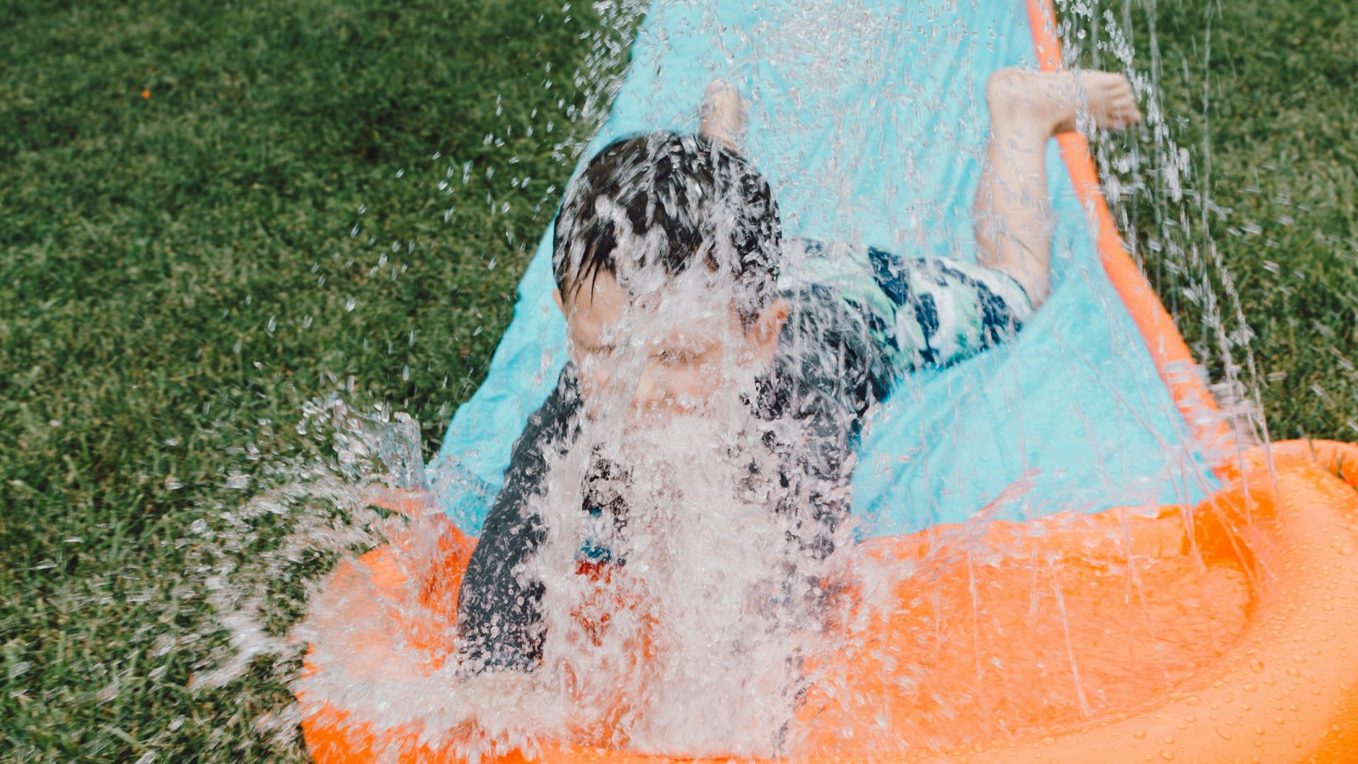 child sliding on blue and orange slippery pad with water splash at daytime