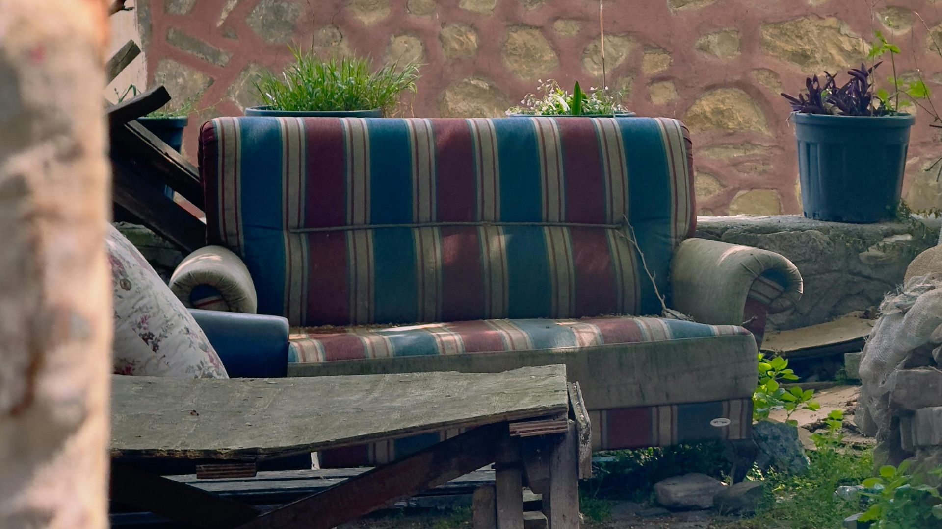 Charming courtyard view with a vintage striped couch and rustic stone wall in Zeytinbağı, Türkiye.