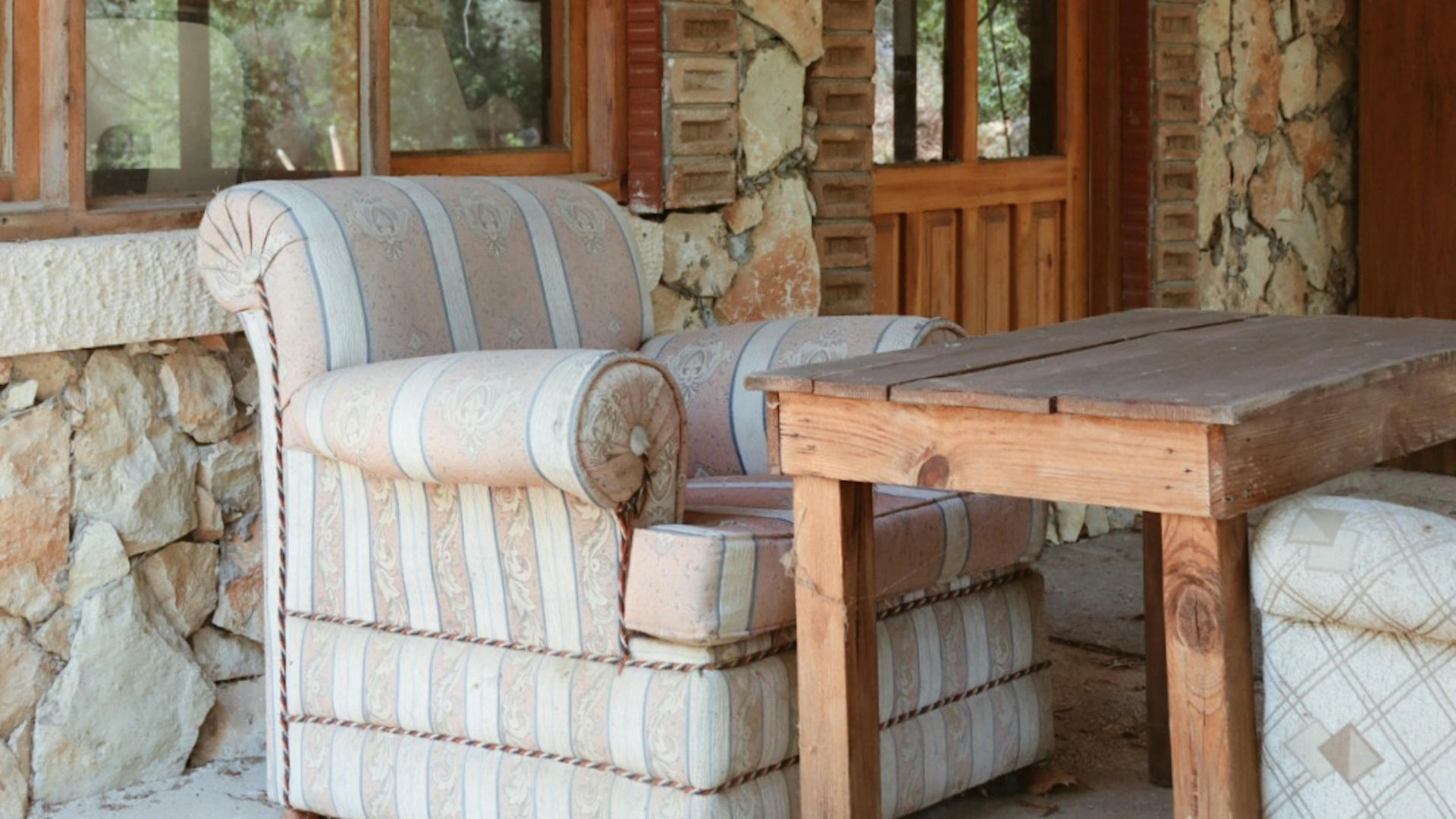 Charming rustic setting with stone walls, wooden table, and a comfy armchair, perfect for relaxation.