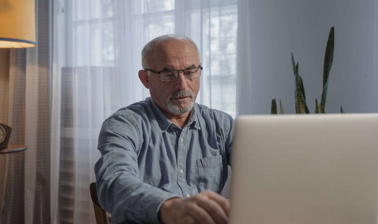 Senior adult man with glasses working on a laptop at home, focusing on online tasks