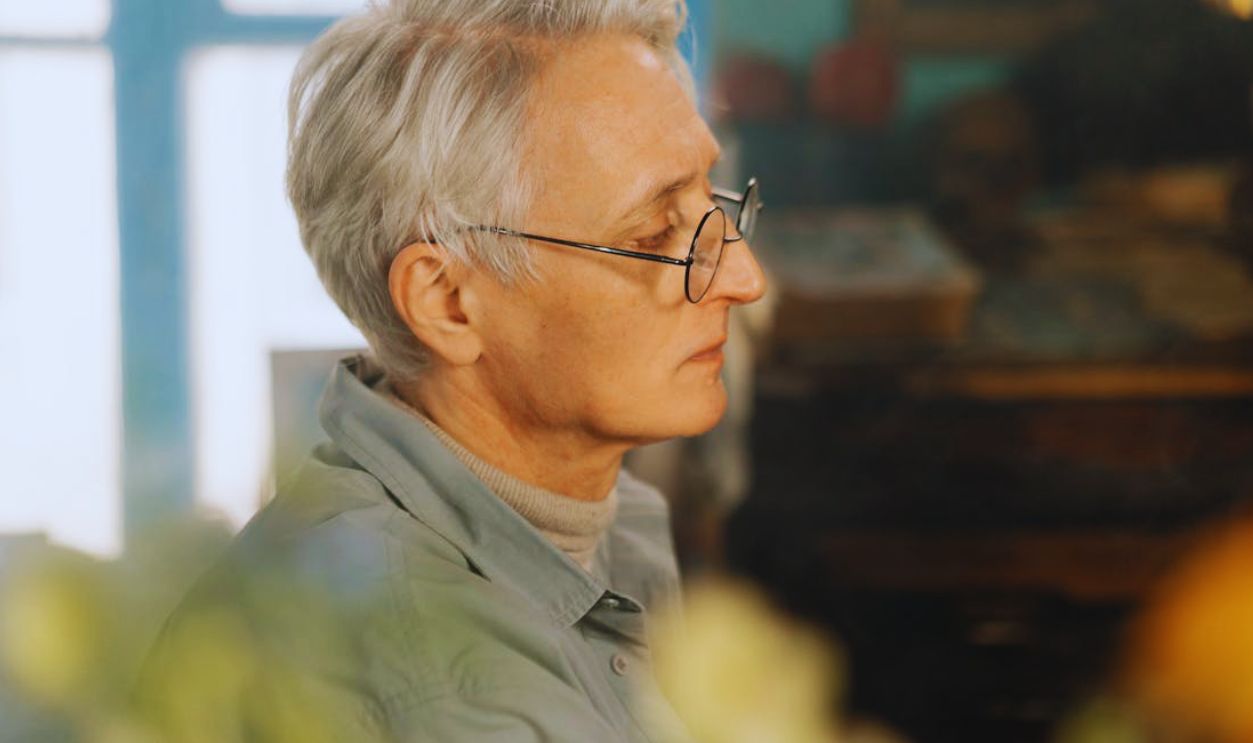 Close-up side profile of a senior man with glasses and gray hair indoors. Warm lighting