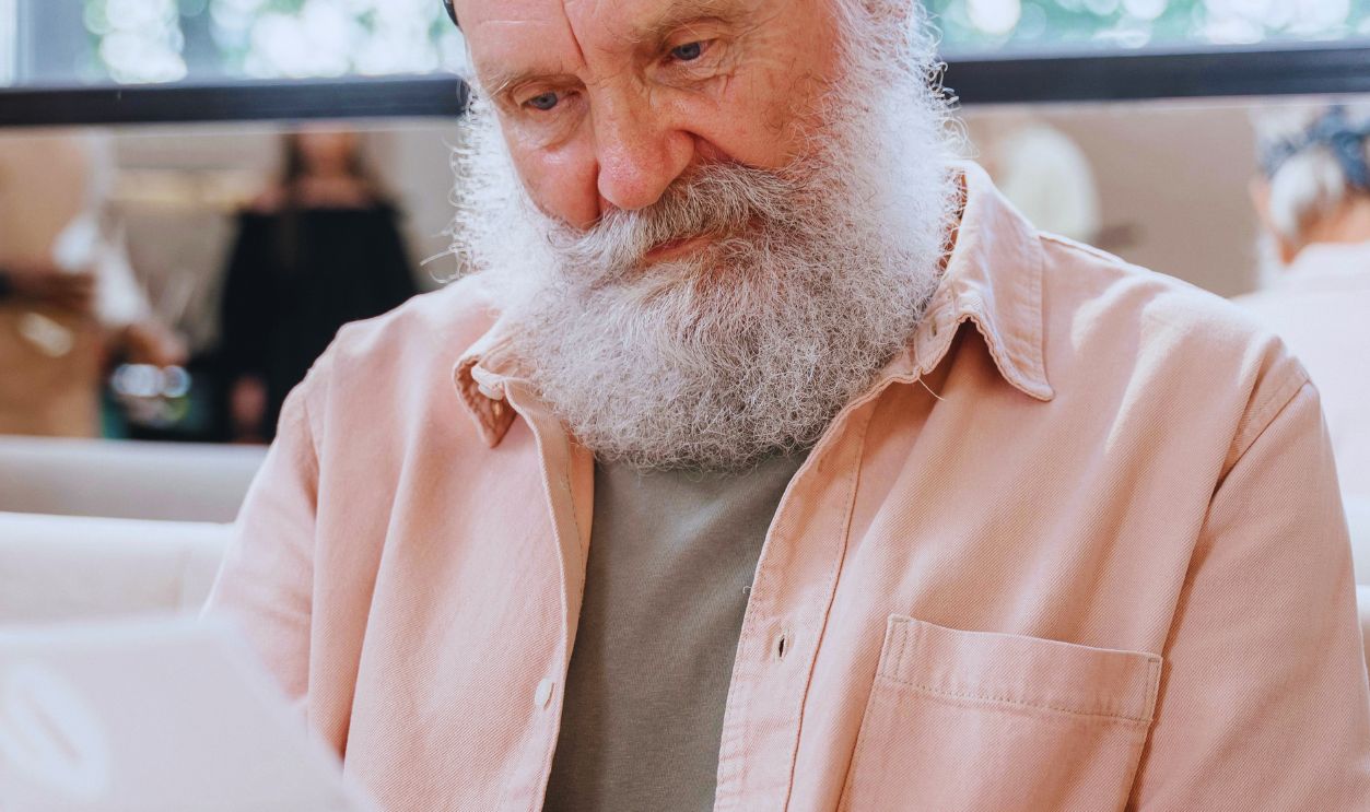 Elderly man with a beard and bandana reading a menu in a cozy cafe