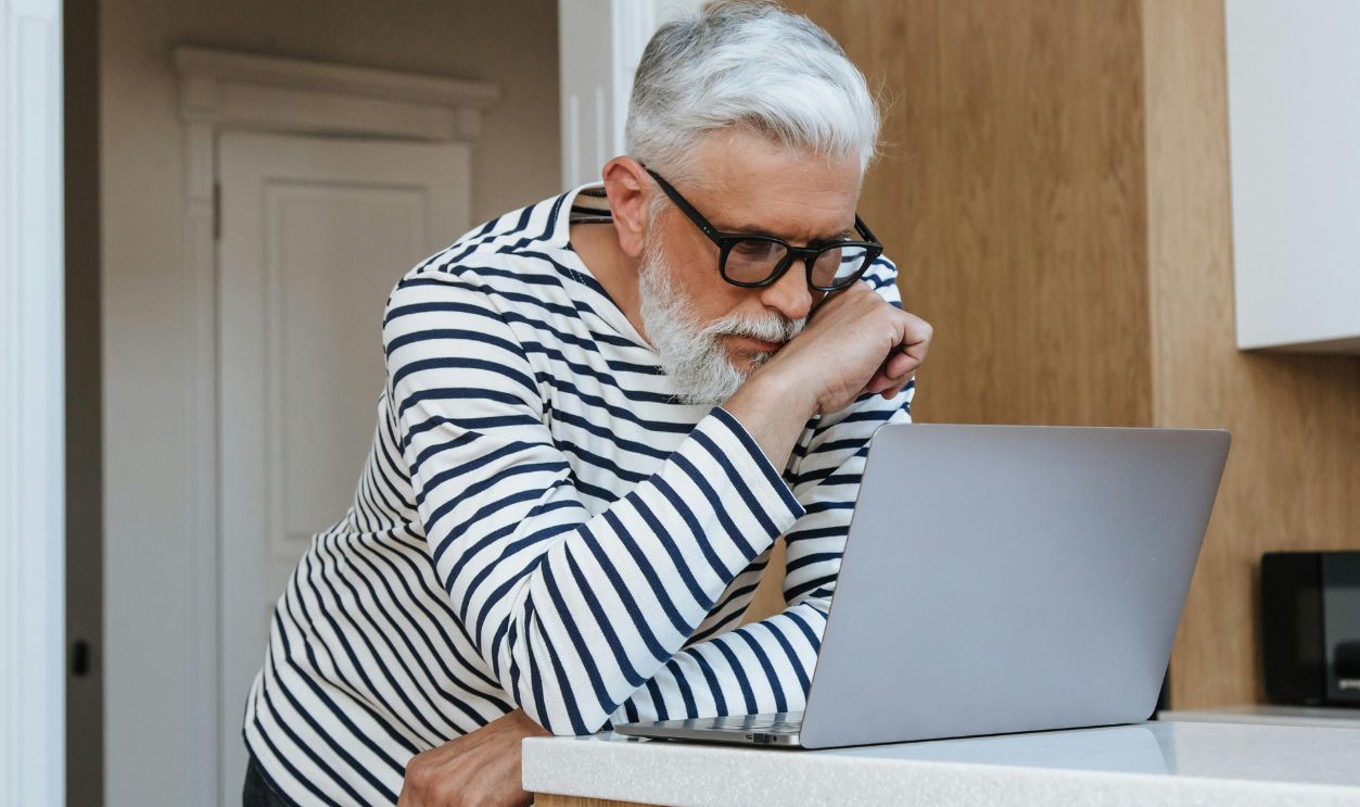A senior adult man with glasses concentrating on his laptop at home, symbolizing modern working environments