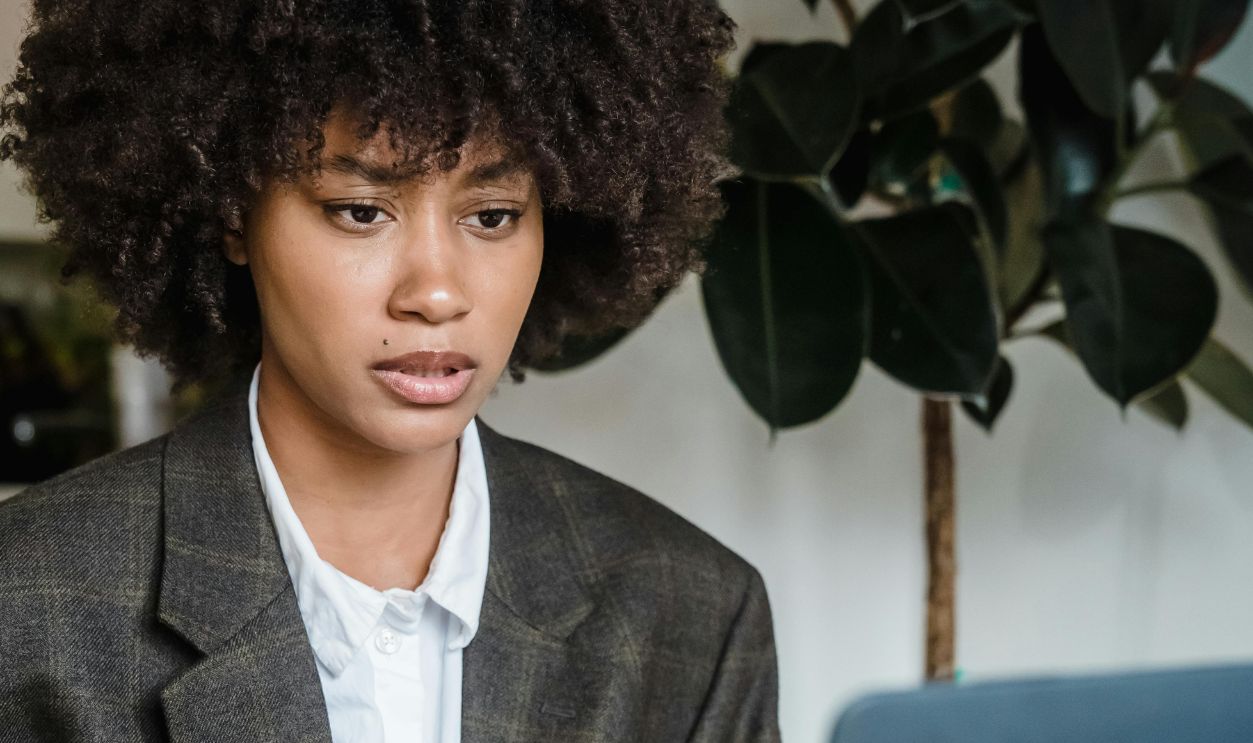 Focused businesswoman with curly hair analyzing work documents on laptop, indoors