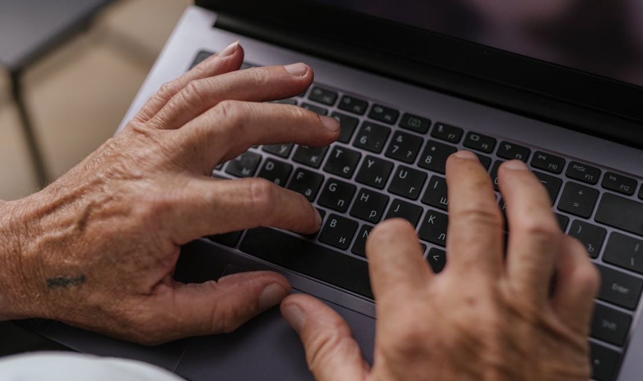 Close-up of senior adult hands typing on a laptop keyboard, viewed from above
