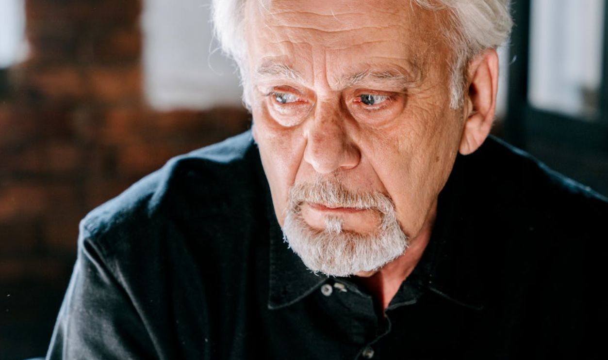 Close-up of a thoughtful senior man in a black shirt, deep in reflection indoors