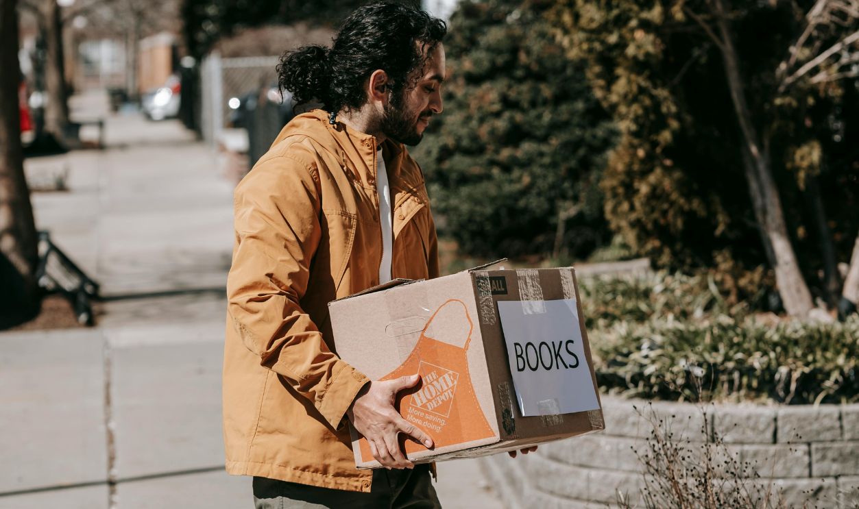 Man carrying a box of books, relocating to a new home in an urban neighborhood