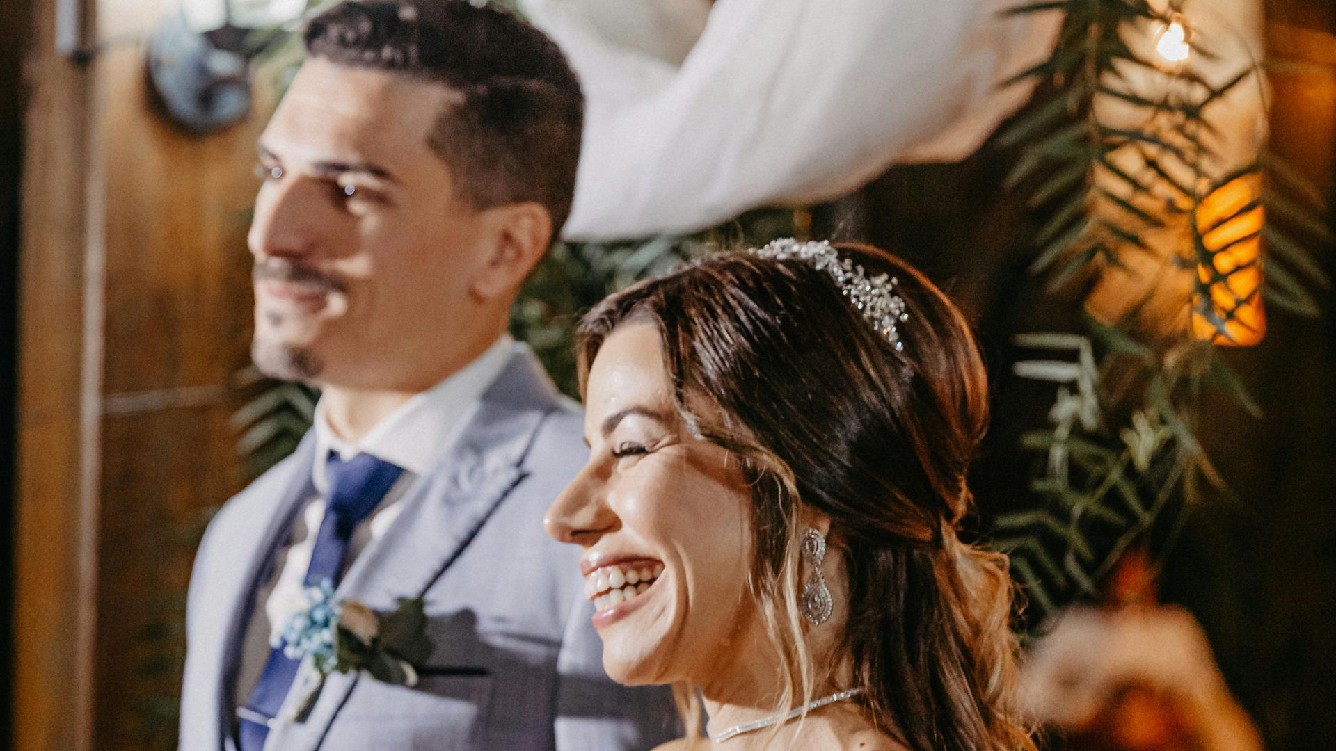 Smiling bride and groom in elegant attire during their wedding ceremony indoors.