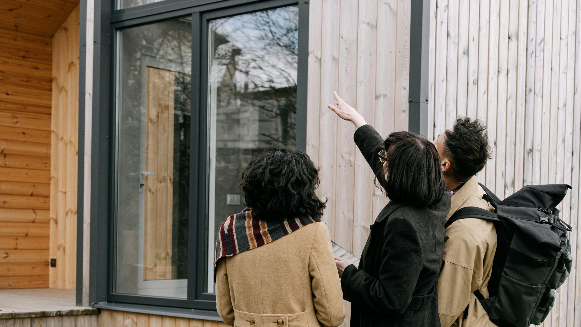 A group of adults inspecting a modern wooden house exterior with a real estate agent.