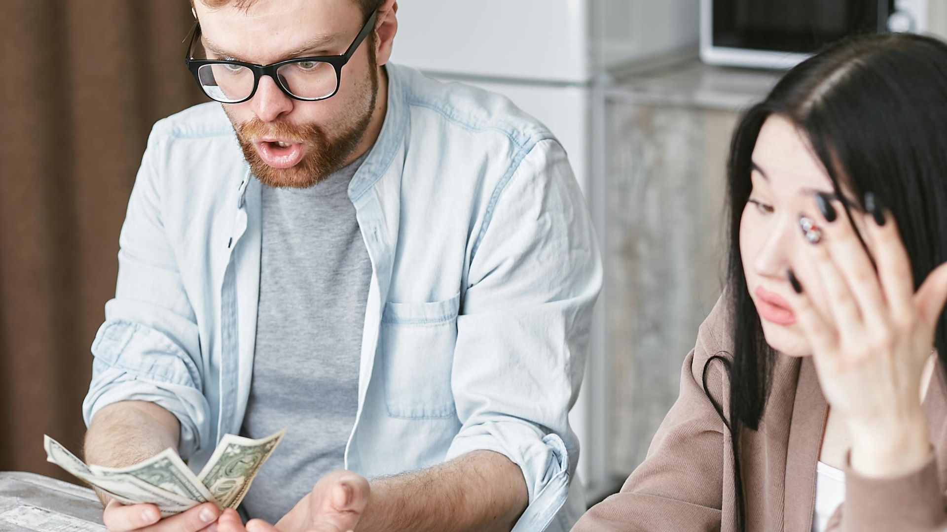 A couple is overwhelmed while handling their finances at home, counting money with stress.