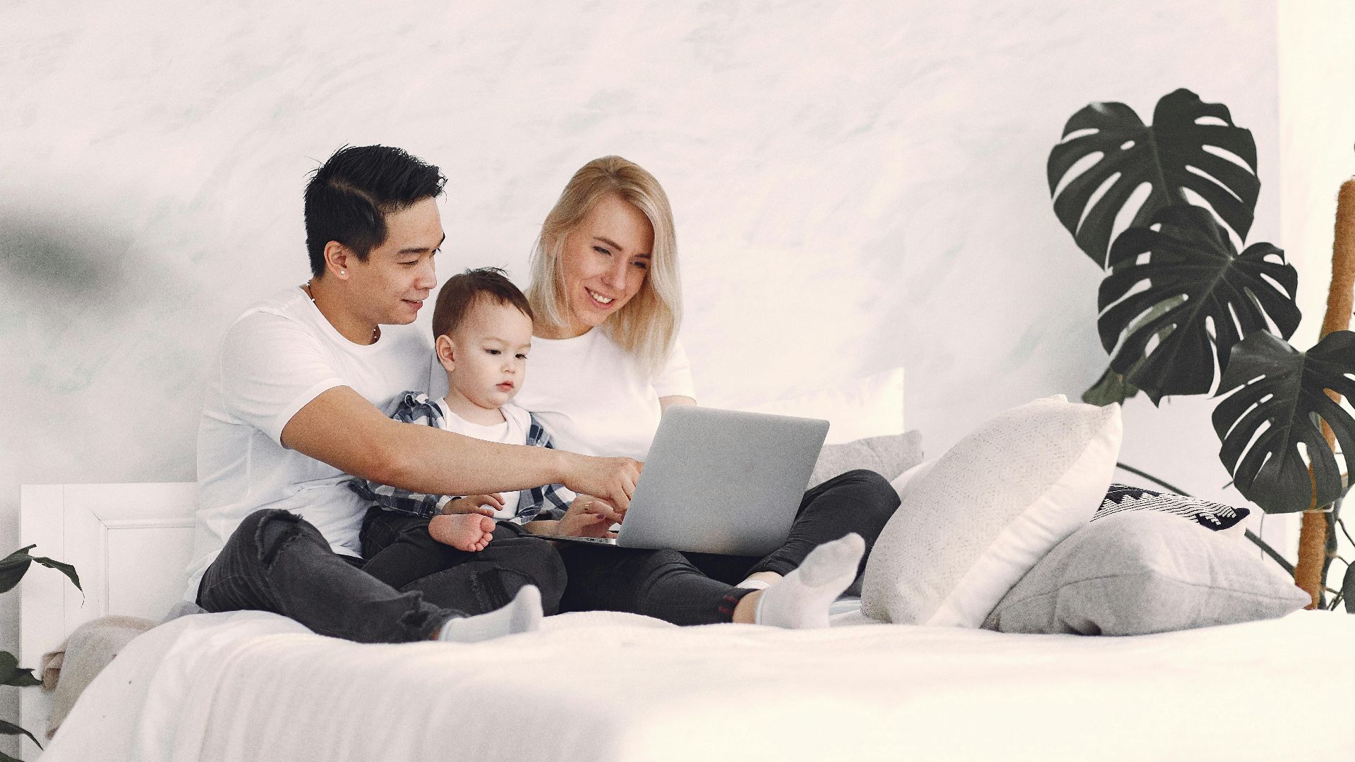 A joyful family with a child enjoying time together on a bed, using a laptop indoors.