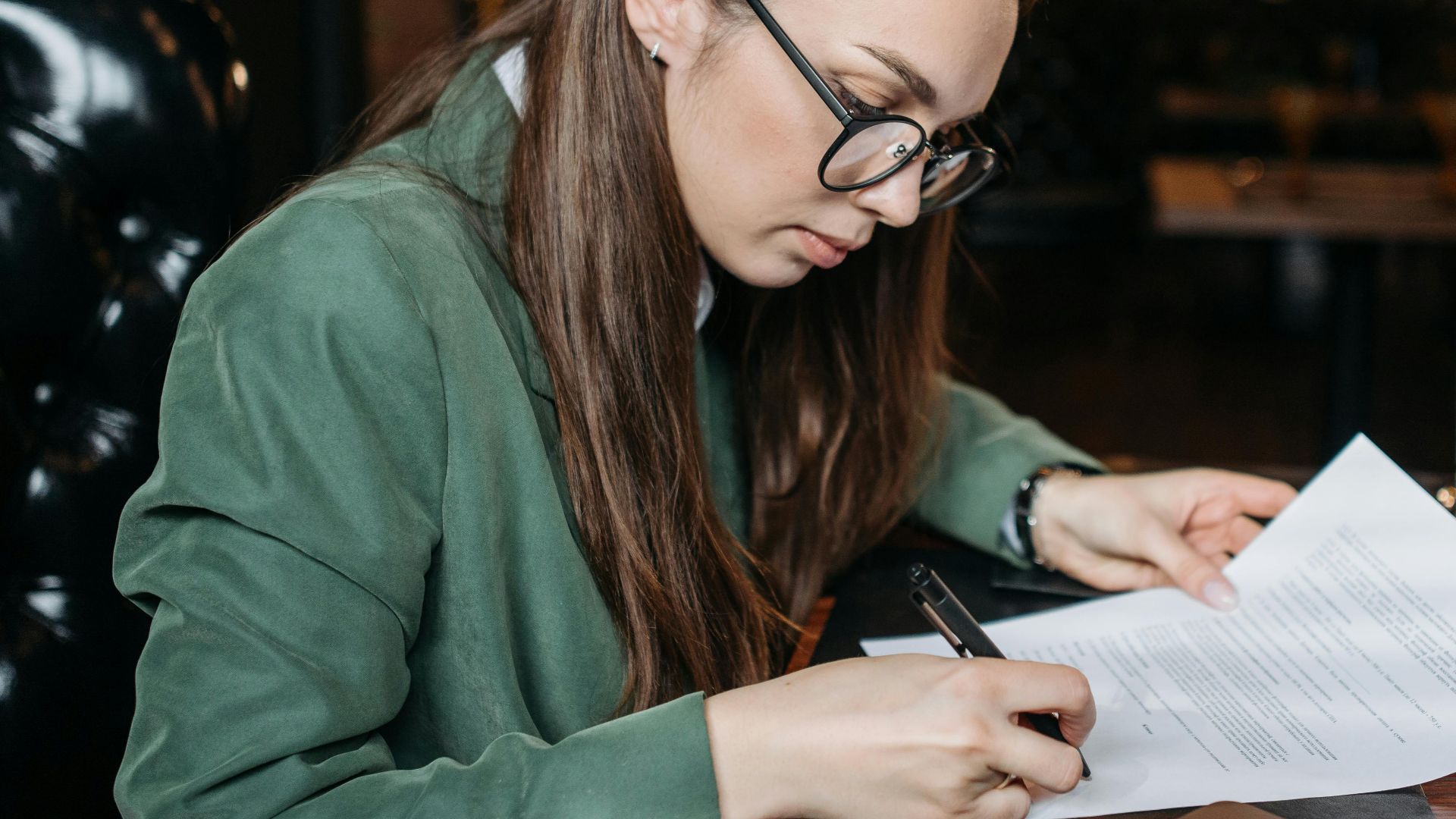 Focused businesswoman in green attire signing important documents at her desk.