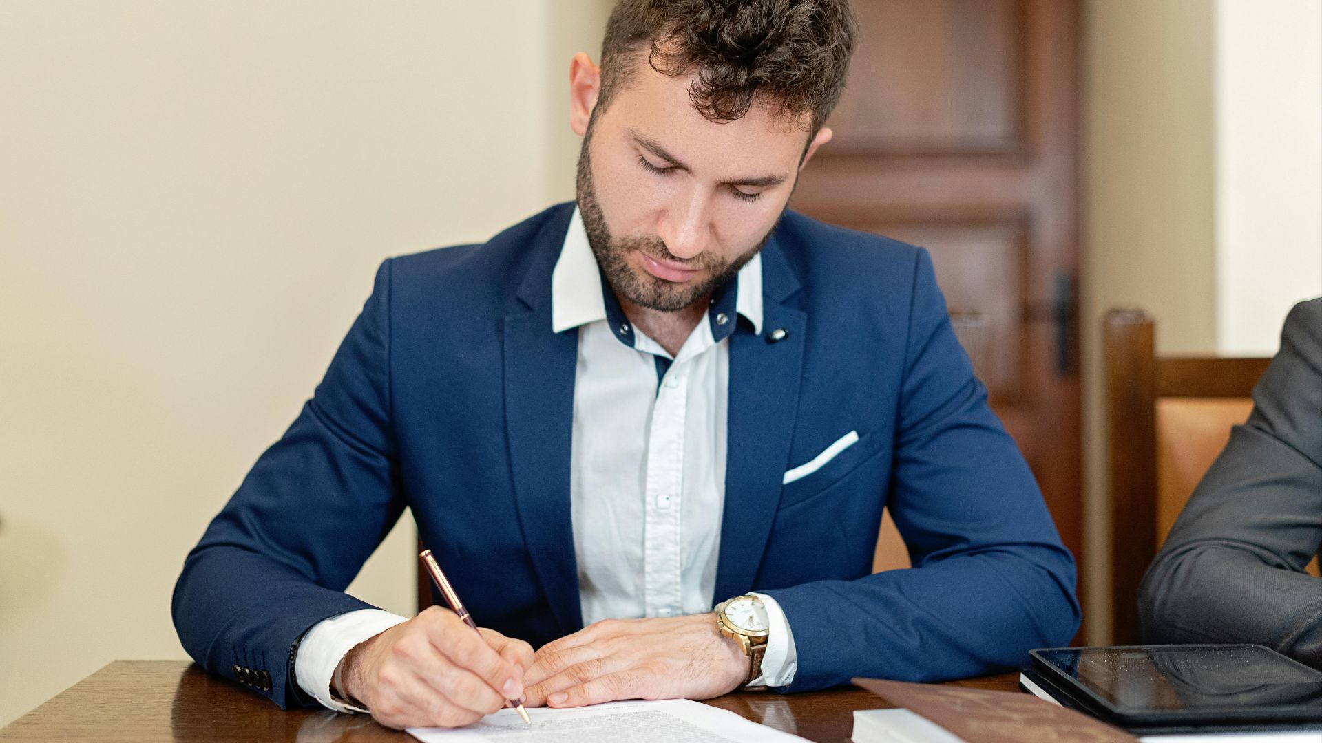 Confident businessman in a suit signing a contract at the office desk.