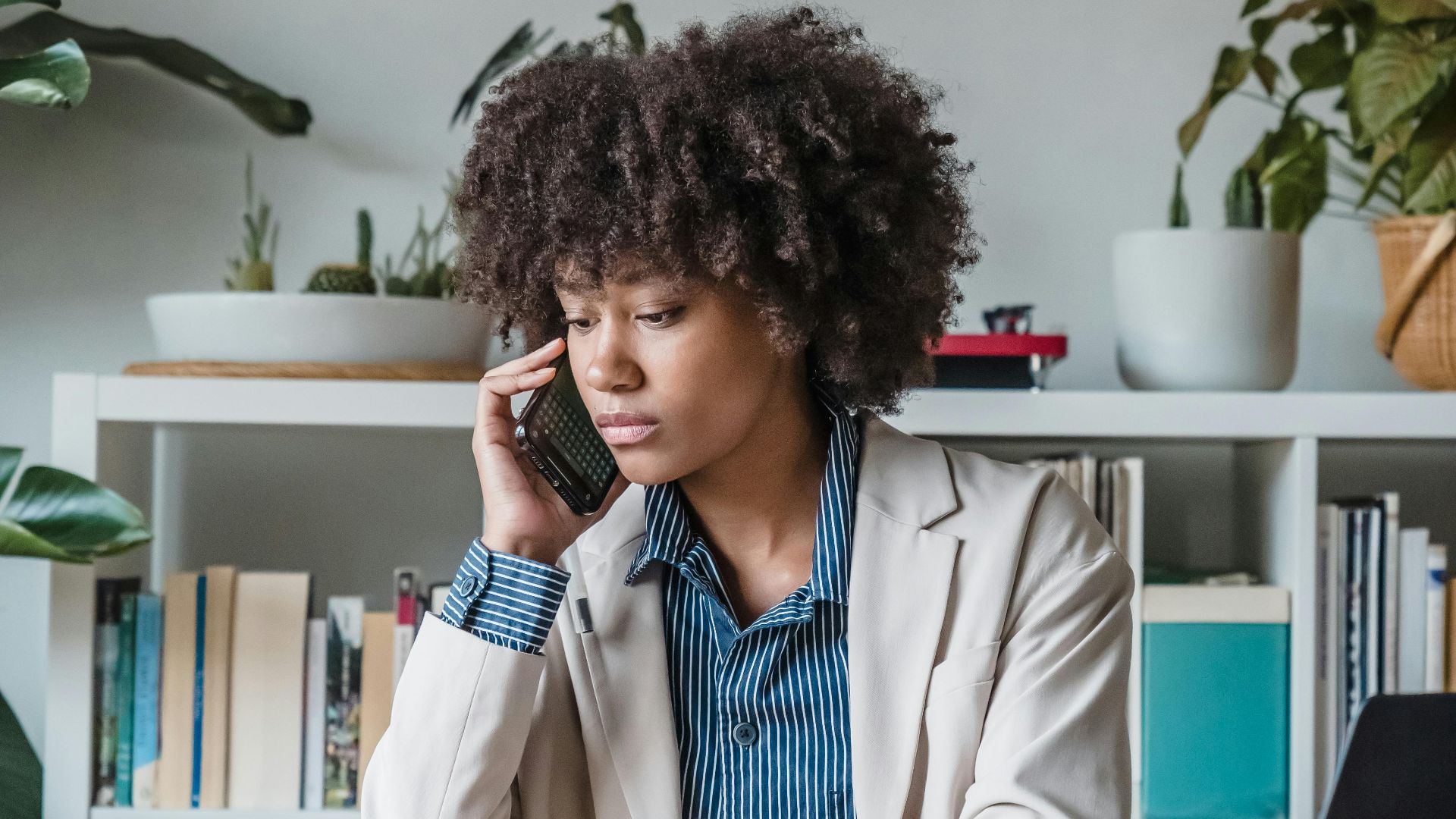 Professional woman multitasking with phone and documents in a modern home office setting.