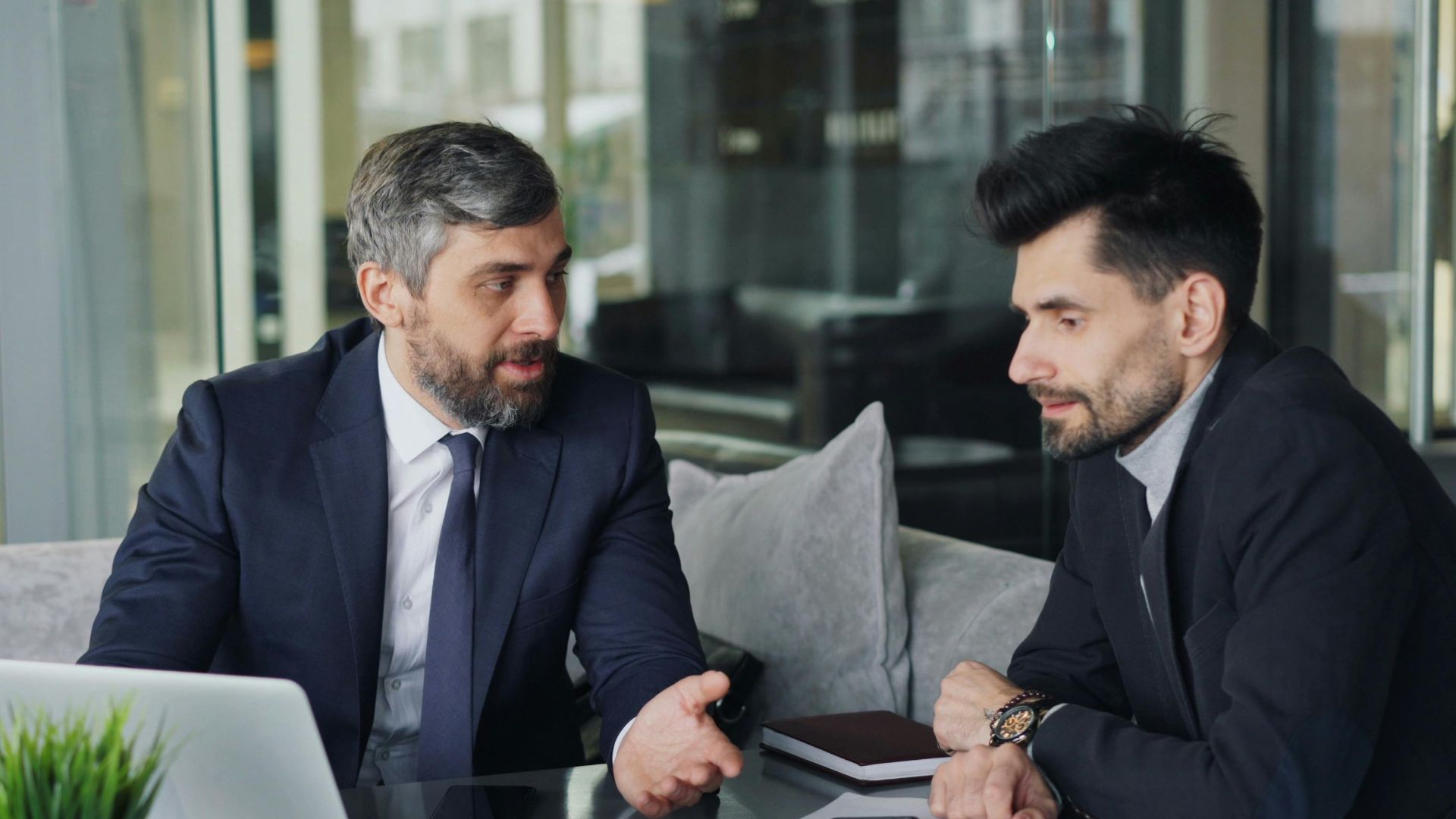 Two businessmen in a café having a professional discussion with coffee and a laptop.