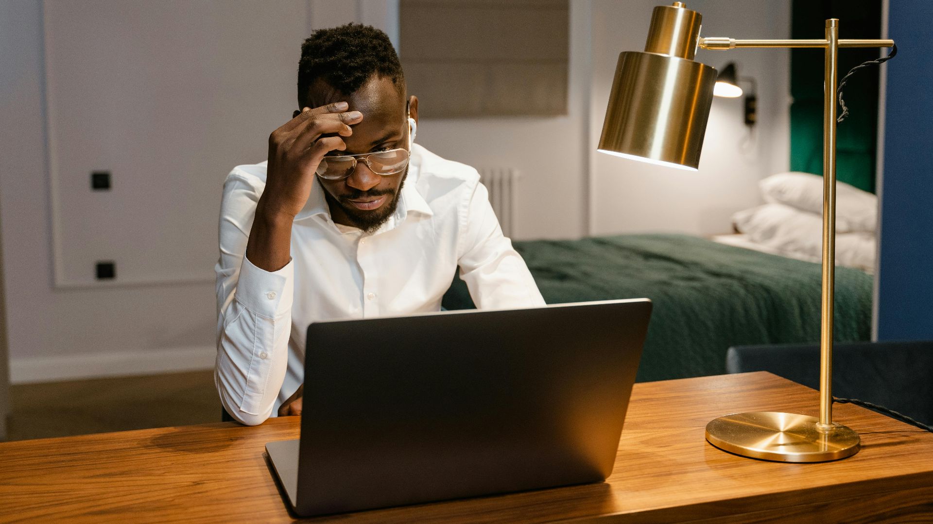African American man working intently on a laptop in a bedroom setting, symbolizing remote work lifestyle.