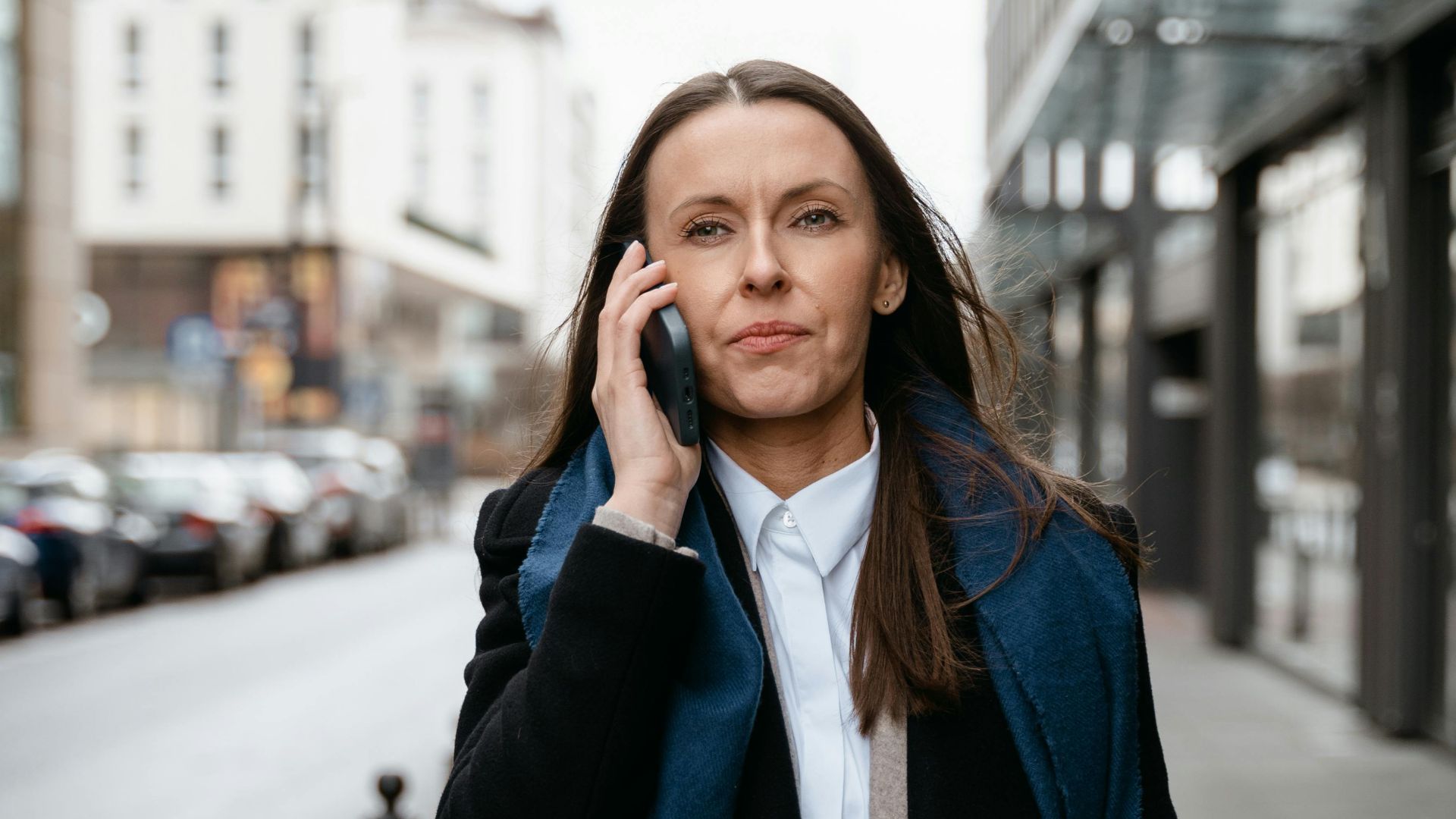 Professional woman walking in urban setting, engaged in cellphone conversation.