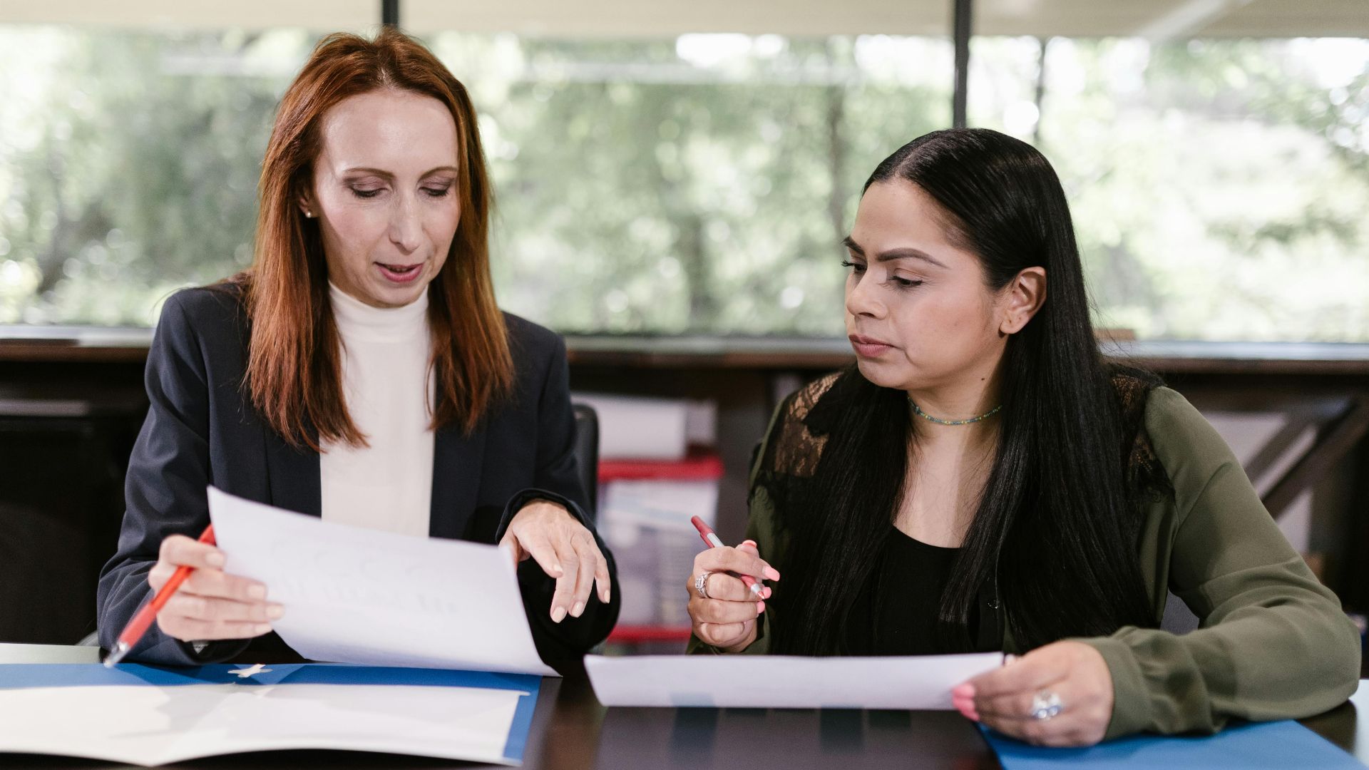 Two professional women reviewing documents in a well-lit office setting.
