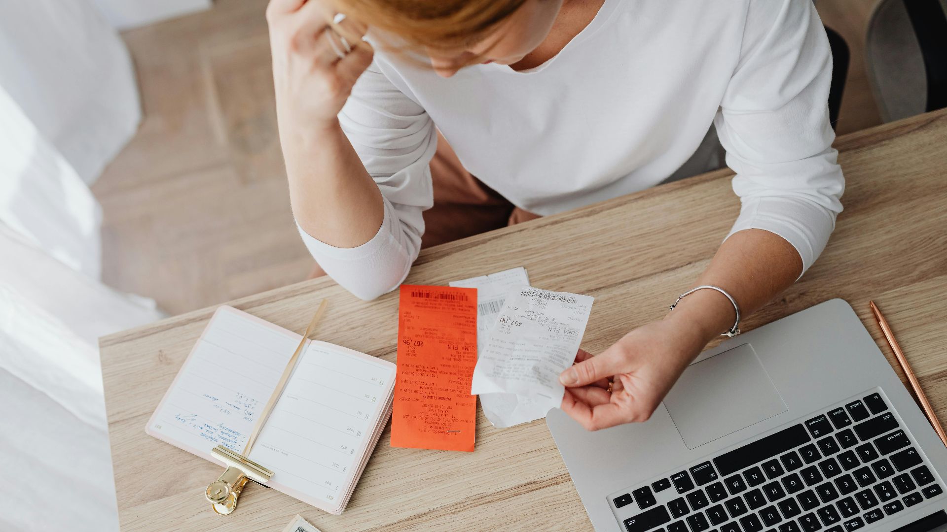 Woman reviewing receipts and planning budget using a laptop and notebook at home to manage expenses.
