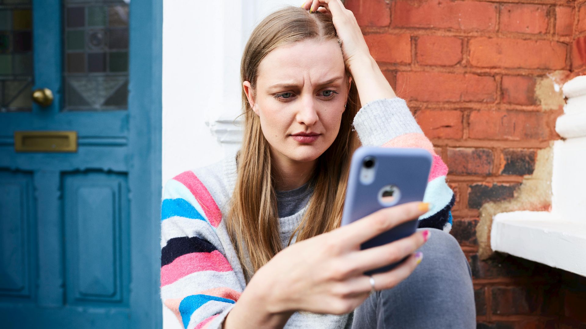 Young woman sitting outside a building, focused on her phone.