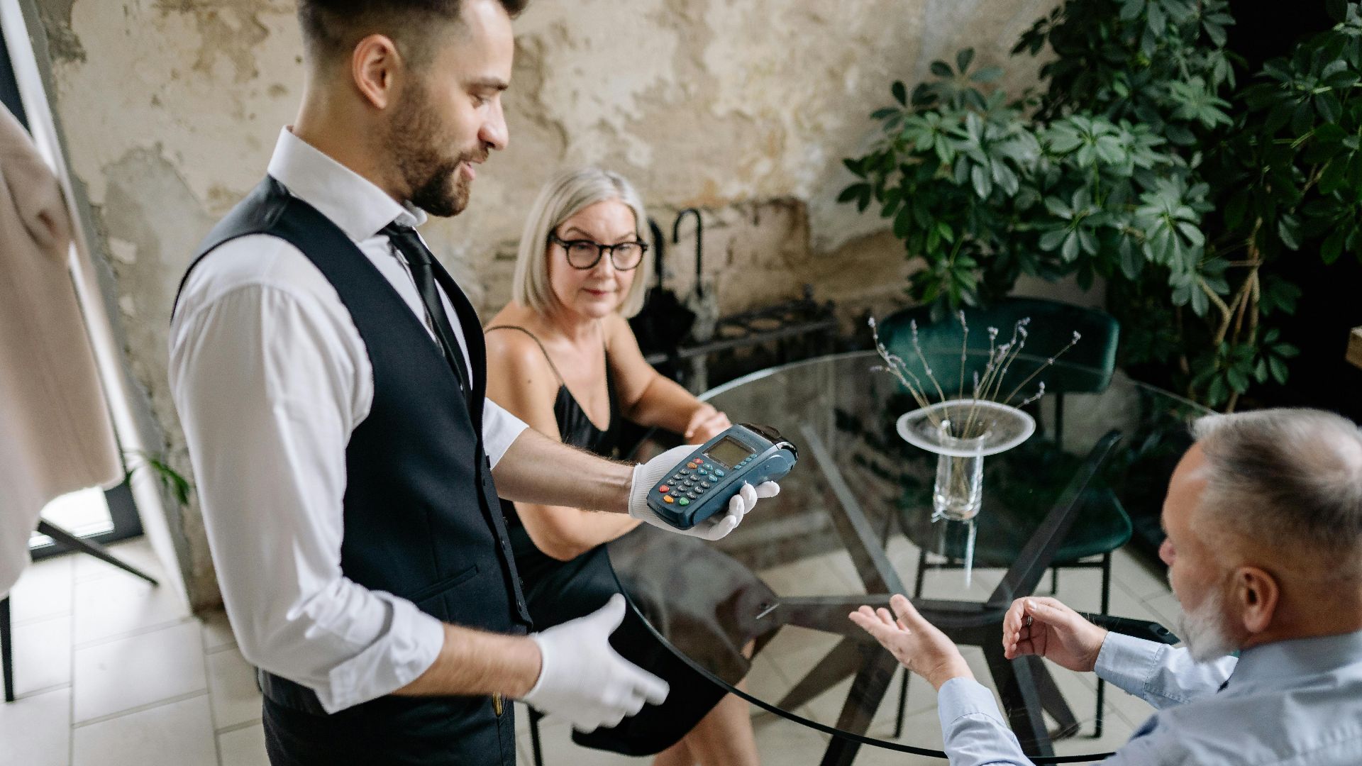 Senior couple completes payment with waiter in stylish restaurant setting, showcasing hospitality service.