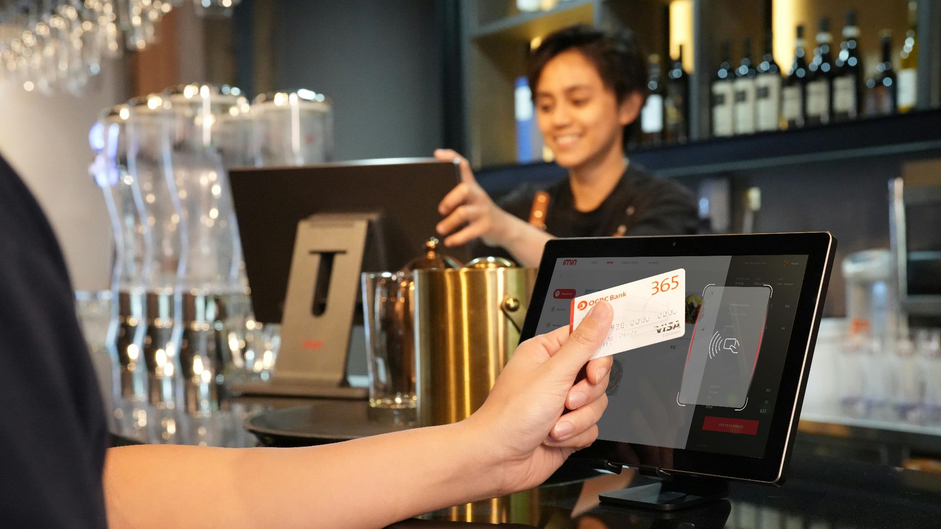 Person using contactless credit card payment at a modern bar, assisted by a cashier.