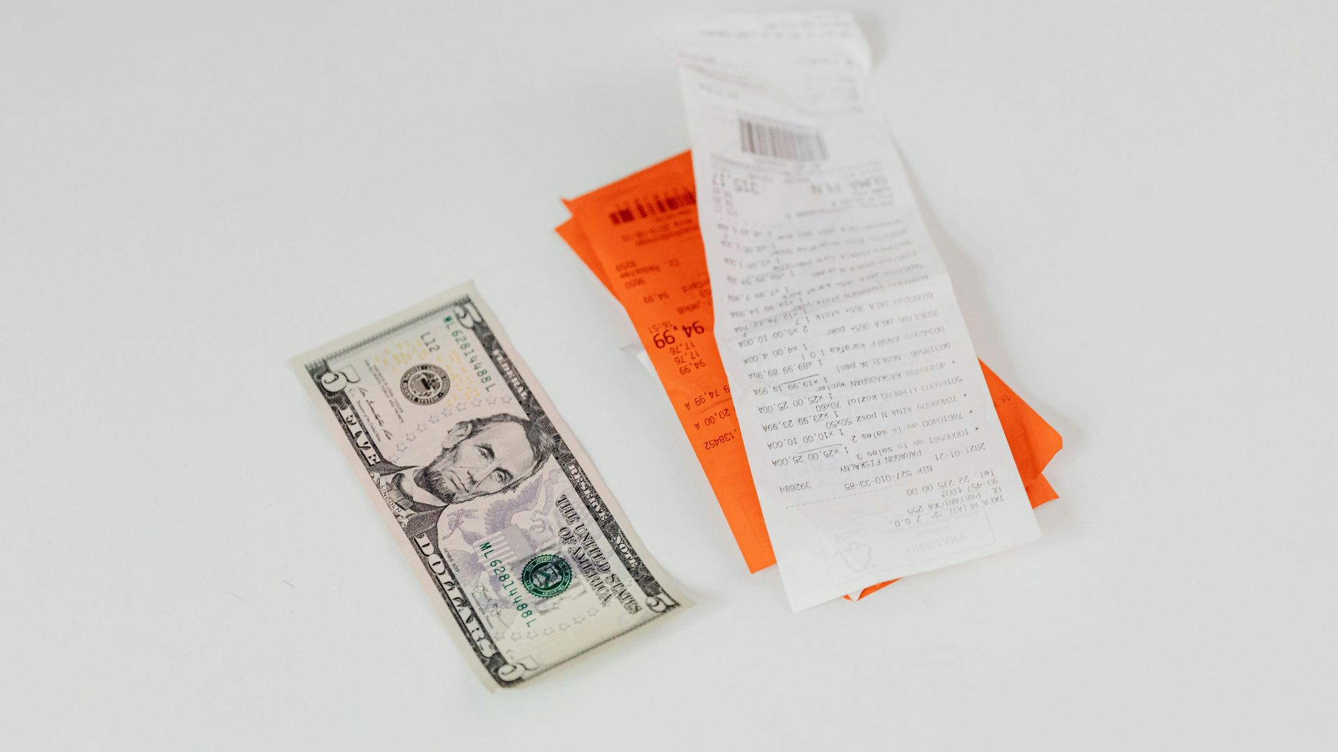 Close-up of a five-dollar bill next to shopping receipts on a white background, ideal for finance and retail themes.