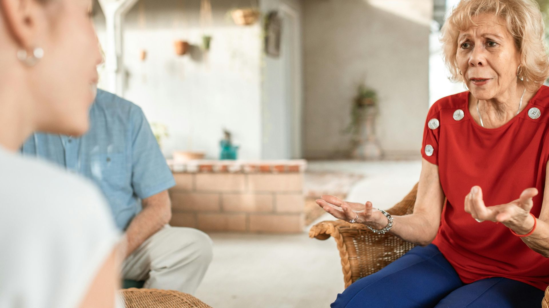 Senior woman in a red shirt chatting expressively with another woman in a cozy setting.