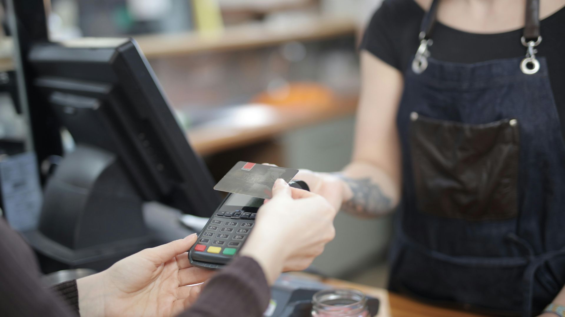 Close-up of customer and cashier during a credit card transaction at a store counter indoors.