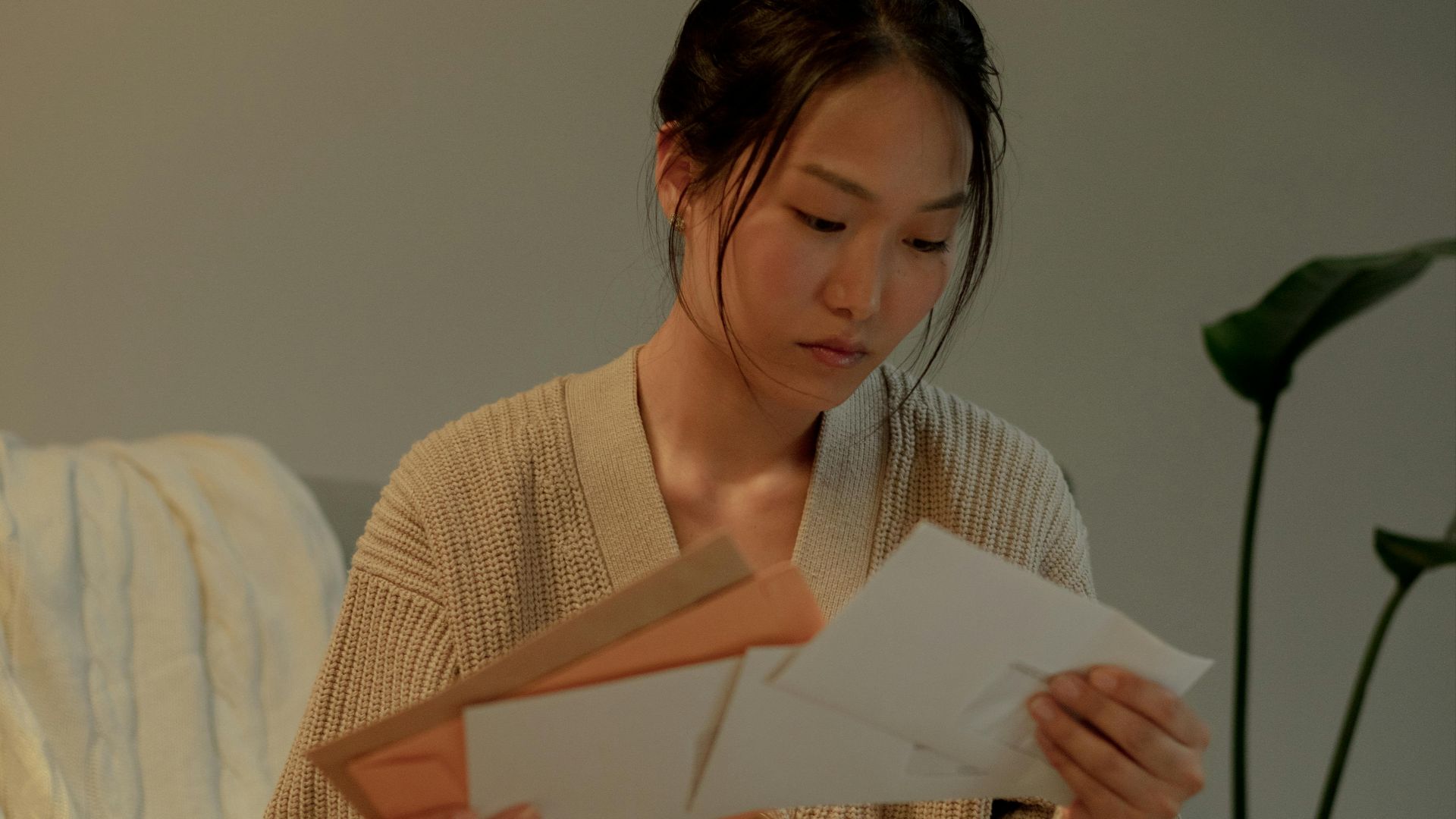 A woman seated in an armchair reads letters with focus, creating a warm, introspective mood.